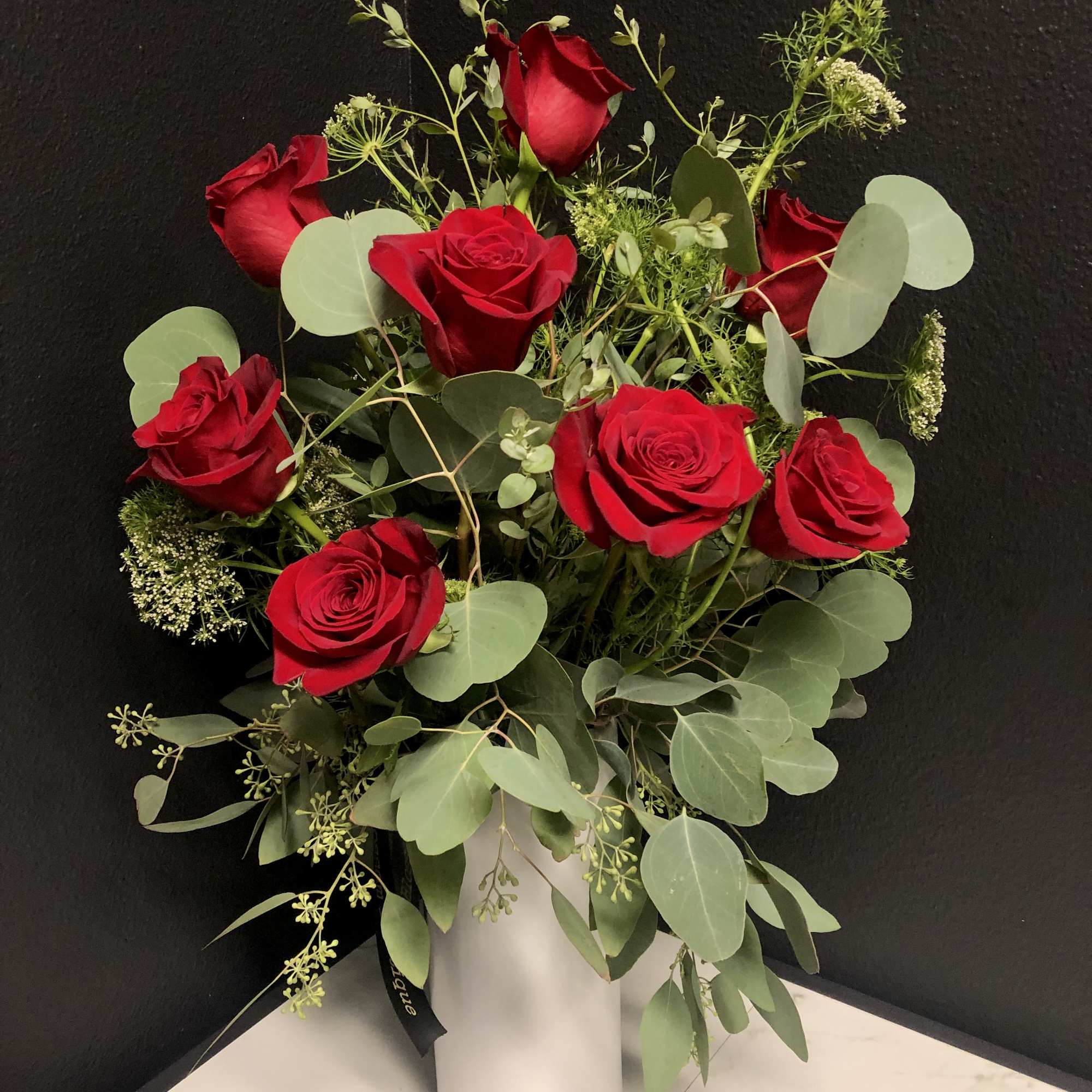Red roses arranged in a white vase with eucalyptus