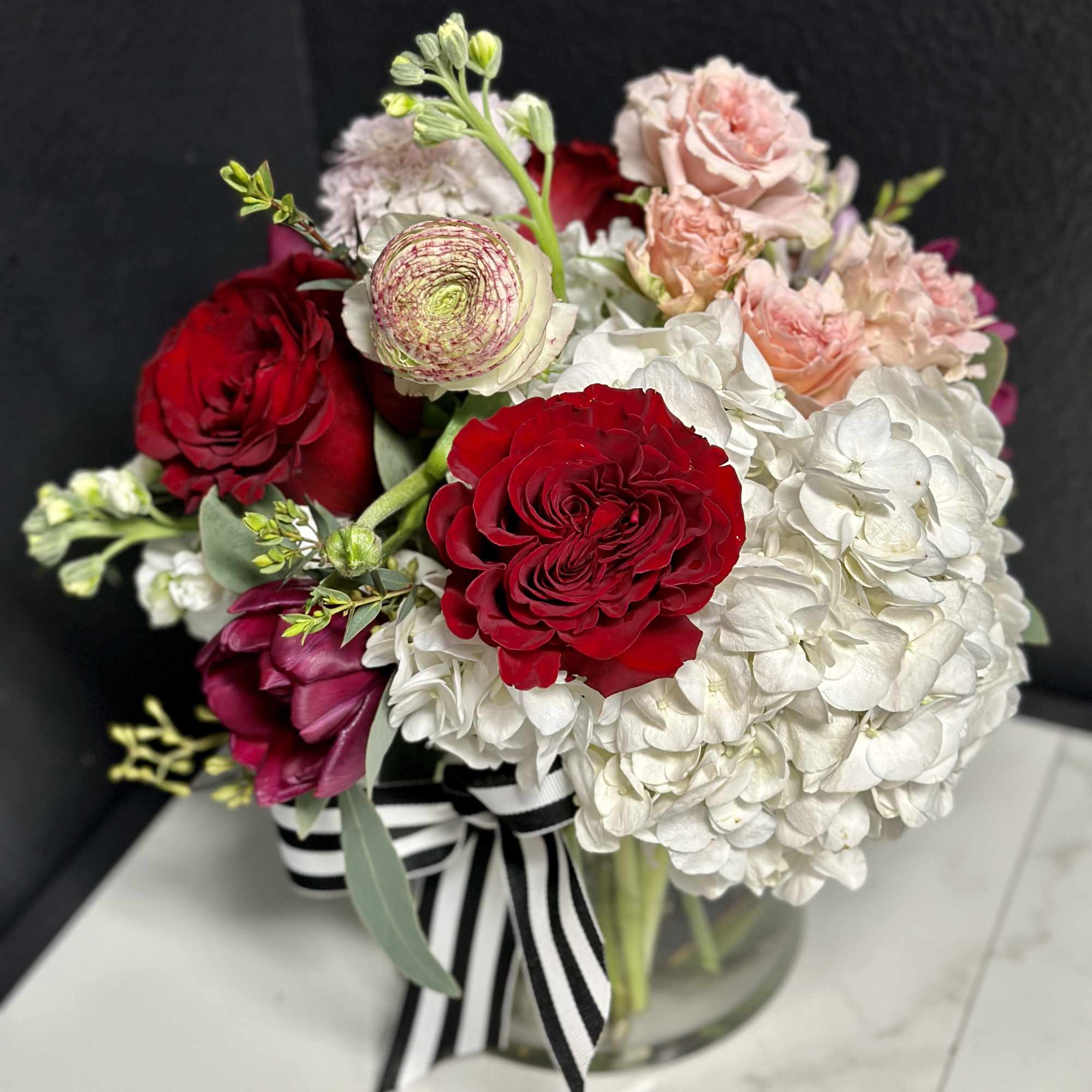 Bouquet of red roses, white hydrangeas, and pale pink blooms in a glass vase