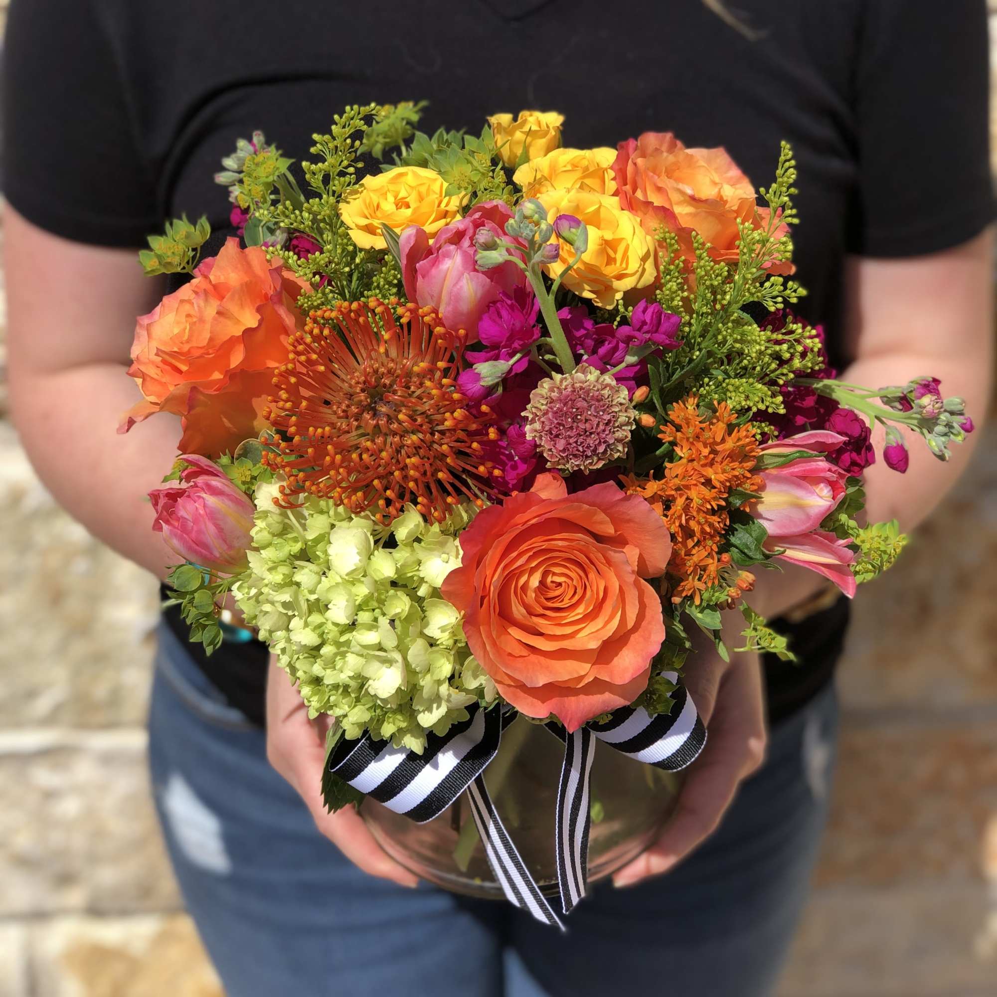 Bright mixed bouquet of orange, yellow, pink, and green flowers in a glass vase