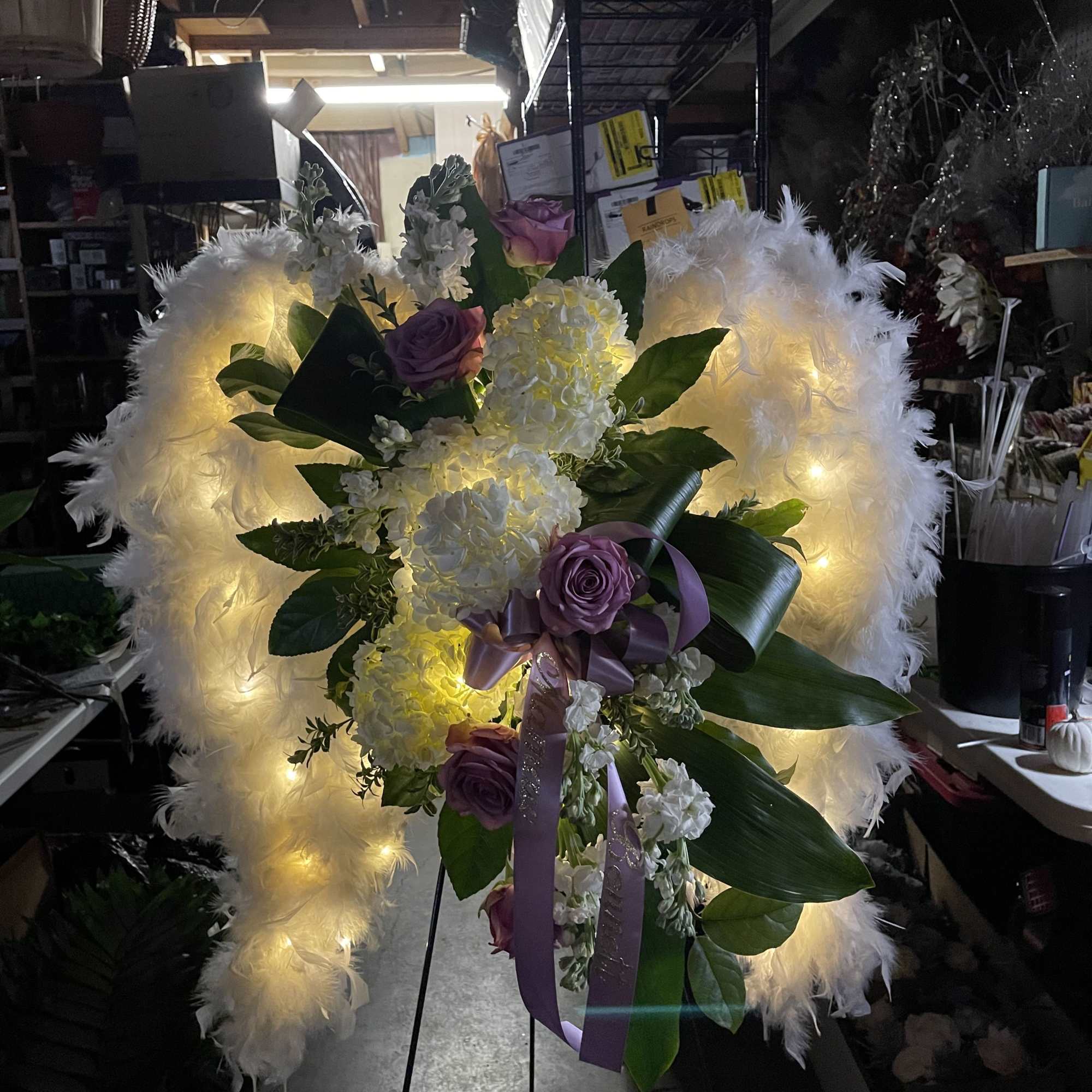 Heart-shaped floral tribute with white lights, purple roses, and white blooms