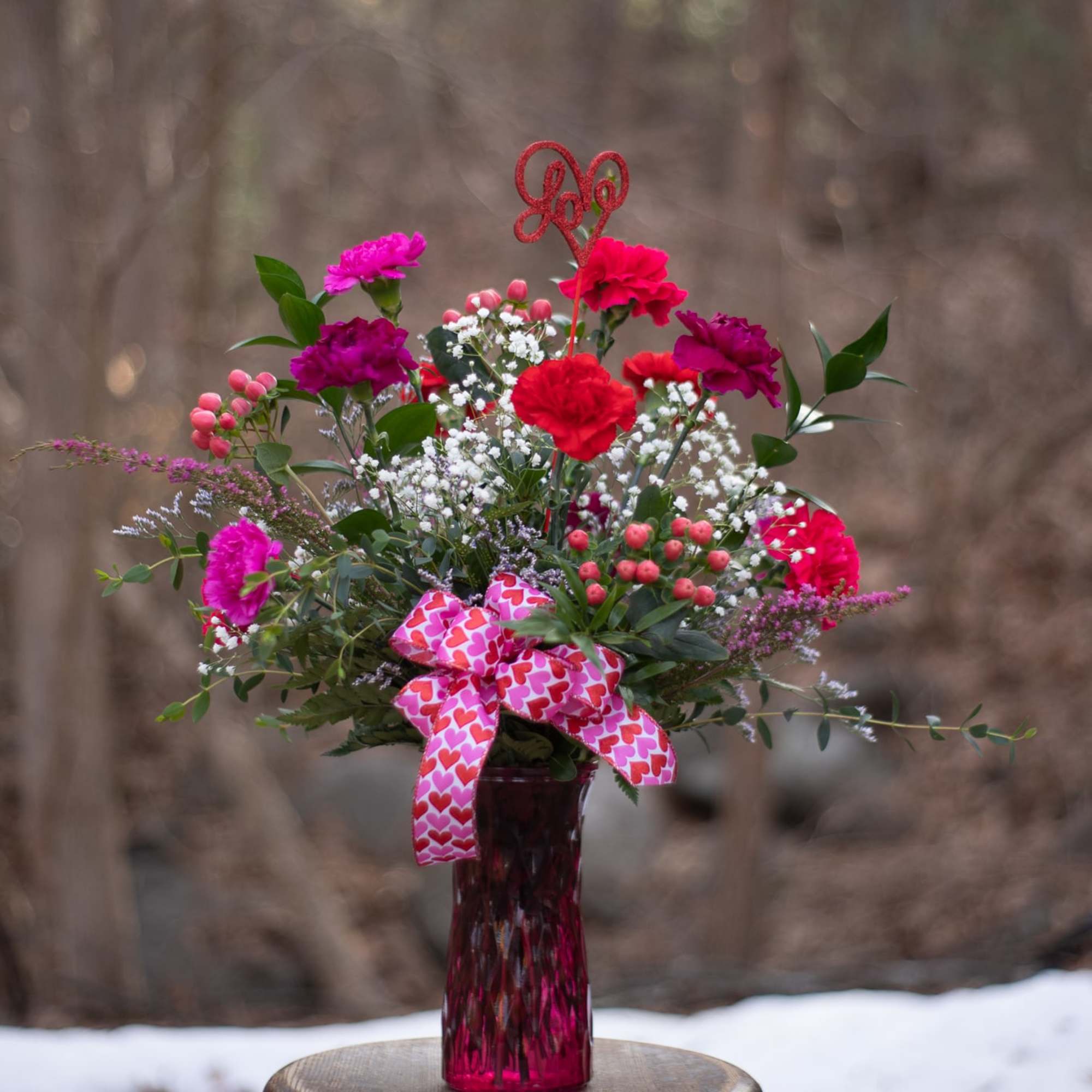 Pink and red carnations in a magenta vase with a heart ribbon