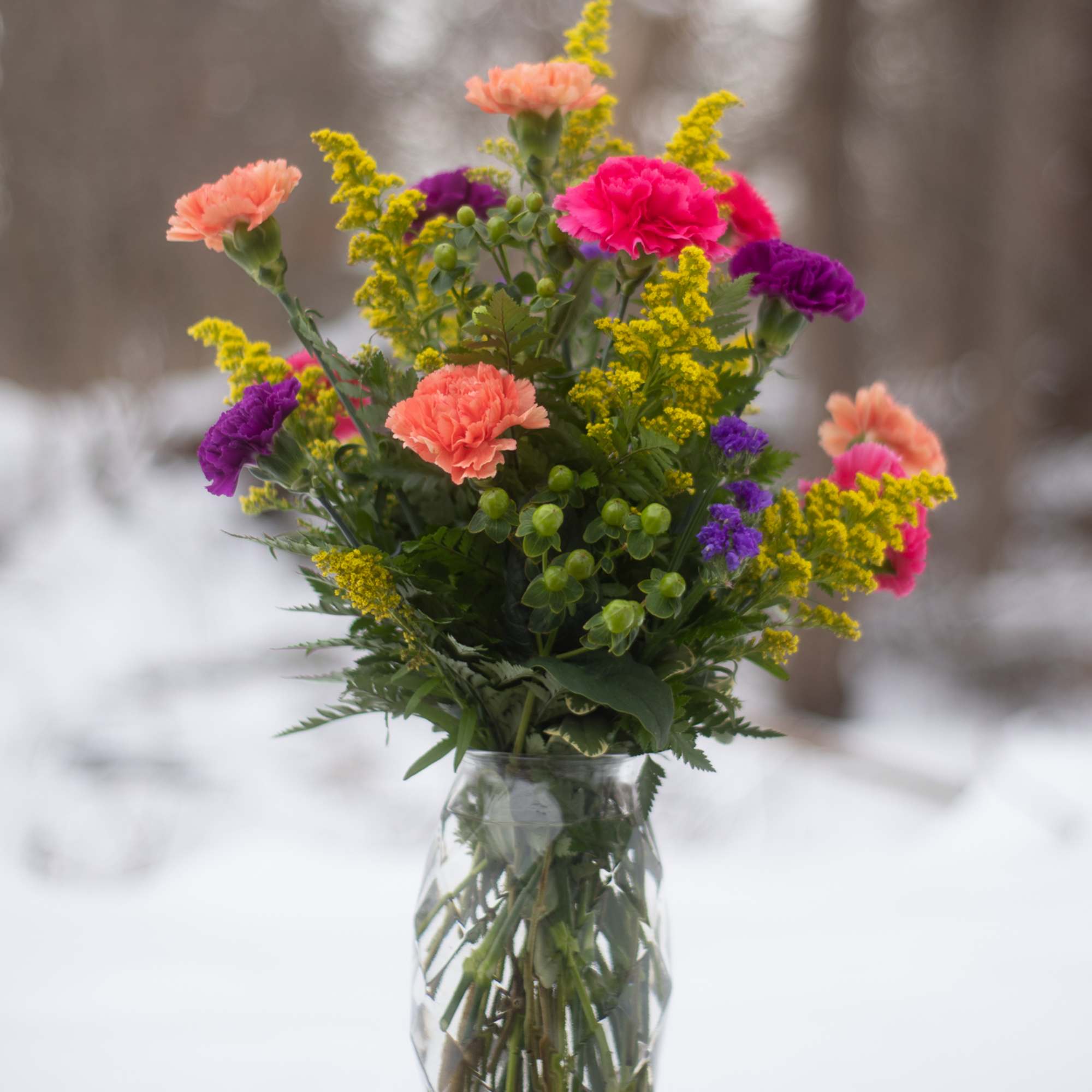 Colorful bouquet of carnations and yellow filler flowers in a glass vase
