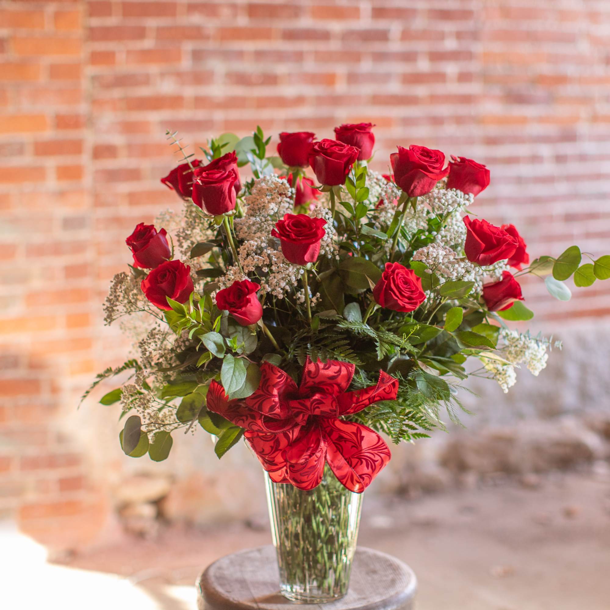 Red roses arranged in a clear glass vase with a red ribbon