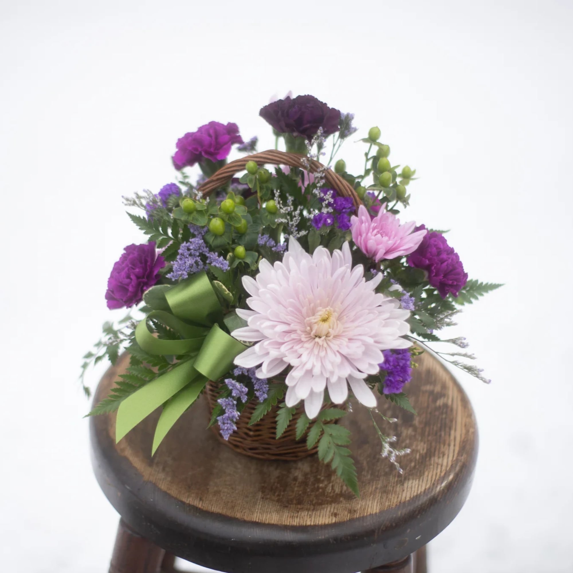 Basket arrangement of pink and purple flowers with a green ribbon