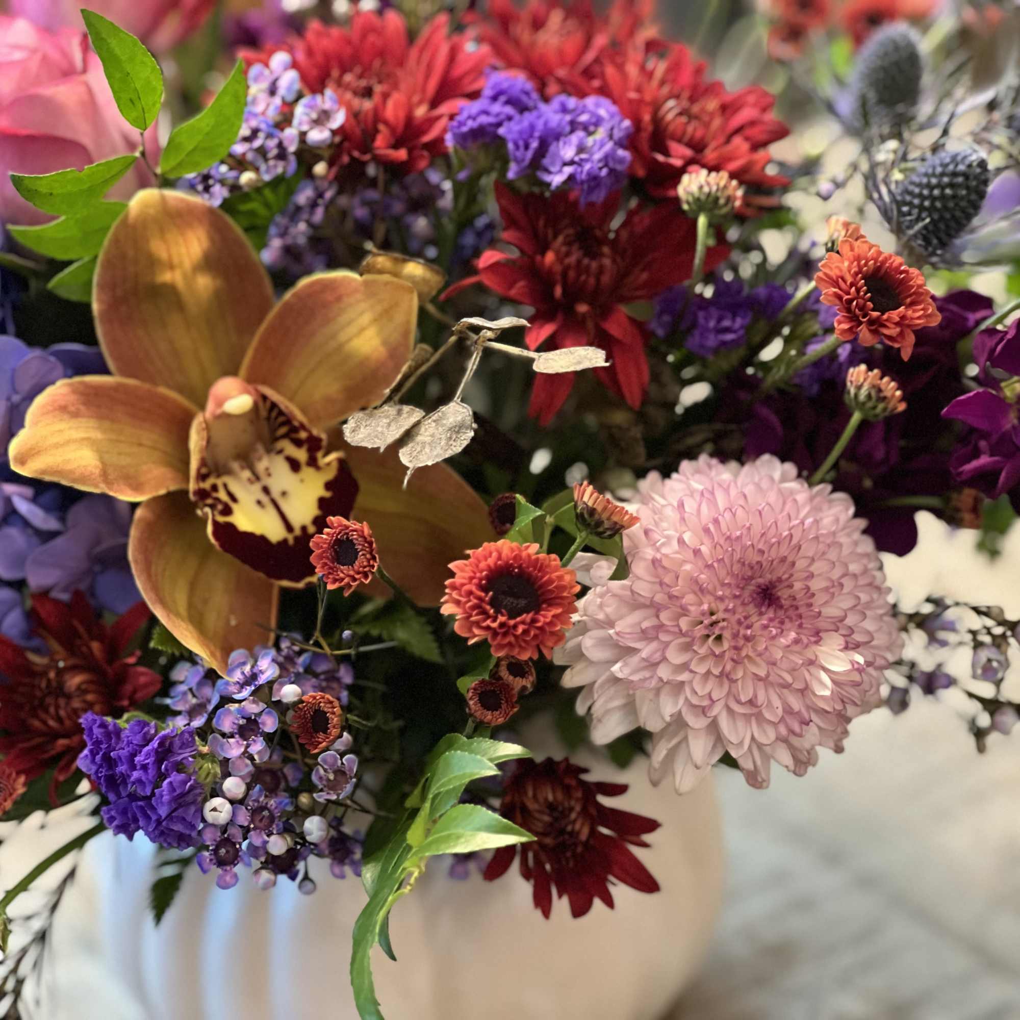 Colorful mixed bouquet with orchids, chrysanthemums, and hydrangeas in a white vase