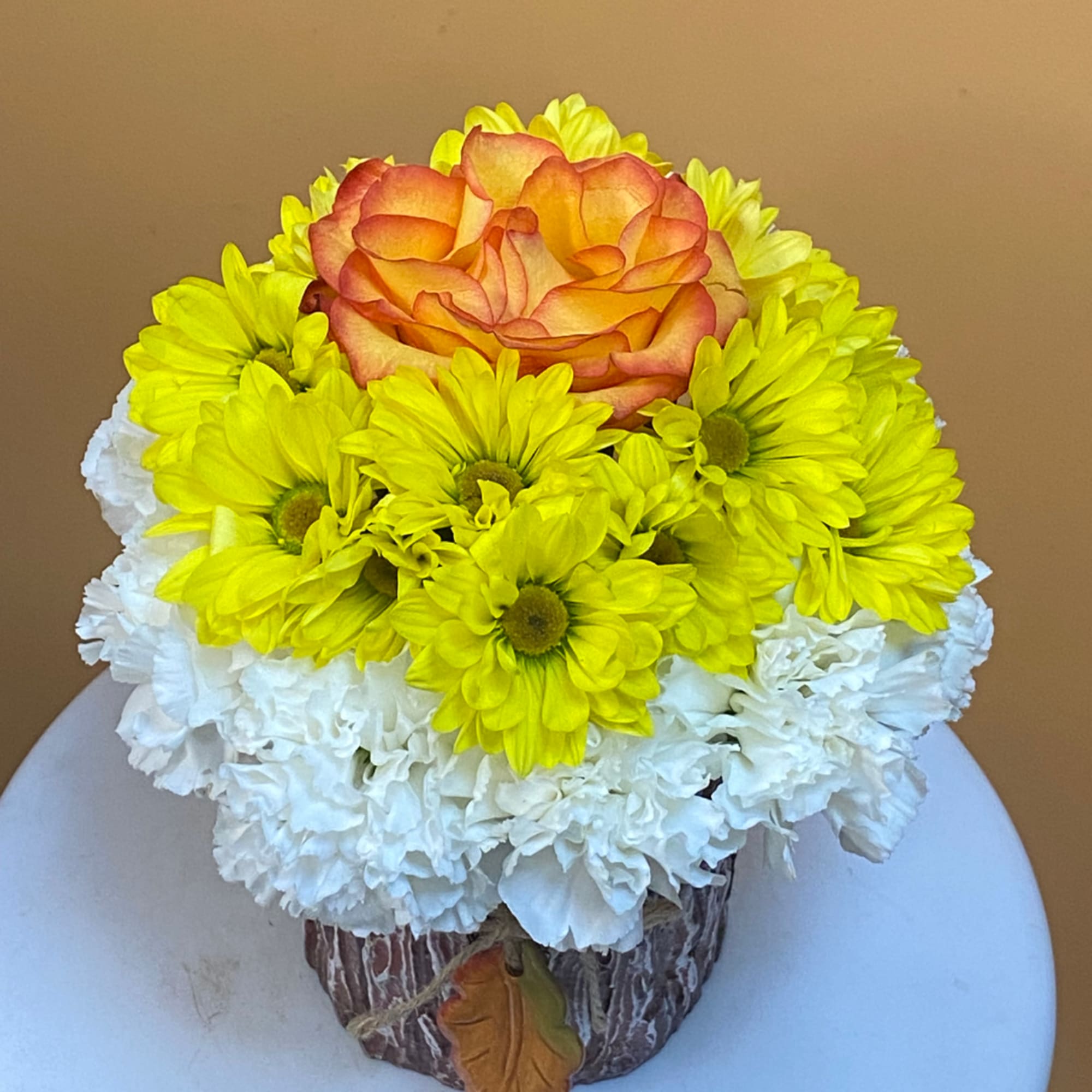 Yellow daisies and a peach rose in a rustic container