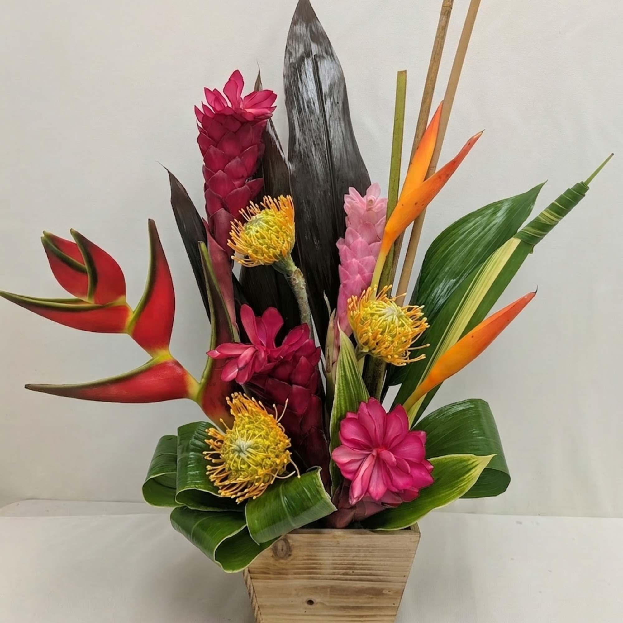 Tropical flower arrangement in a wooden container with pink, orange, and yellow blooms