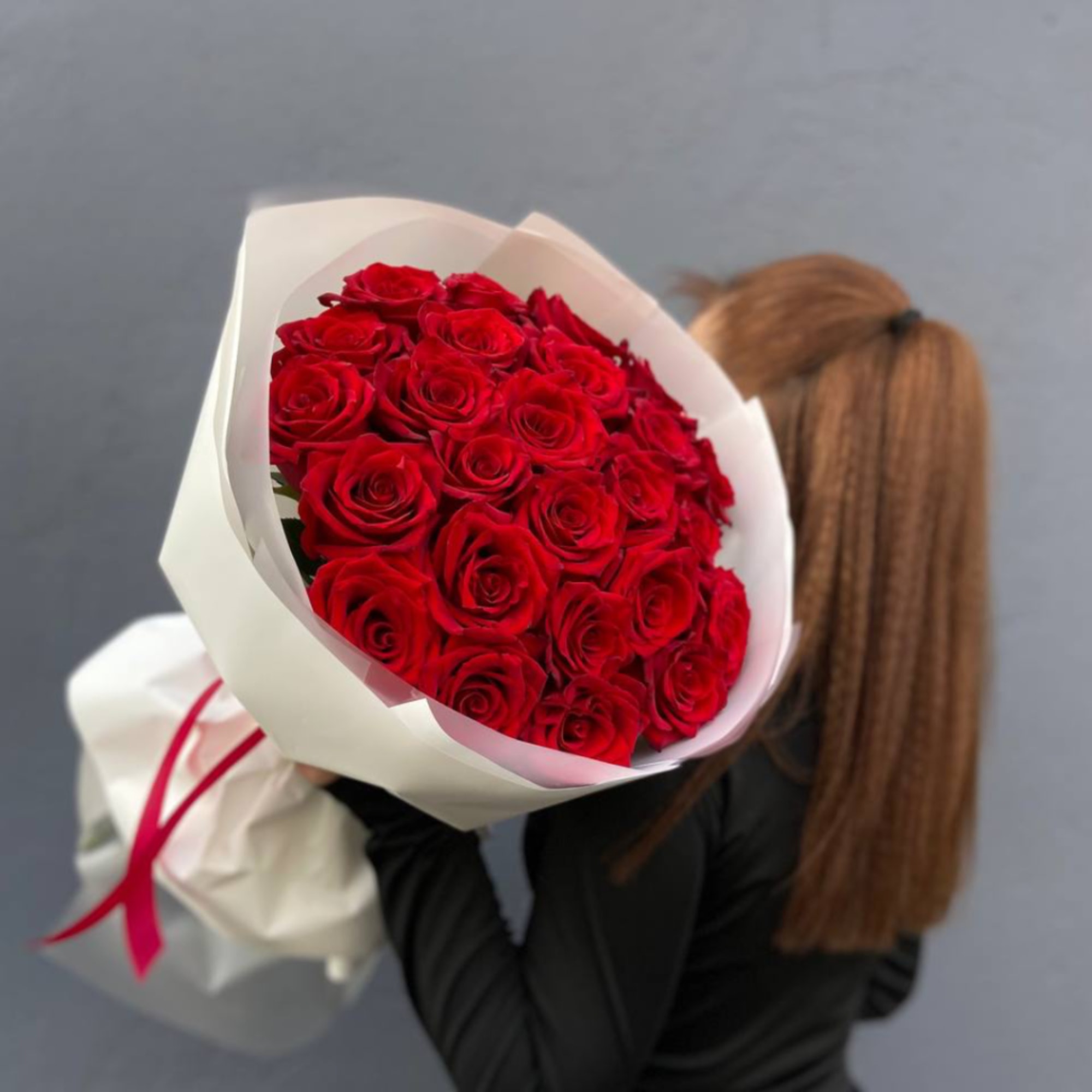 Bouquet of red roses wrapped in white paper with a pink ribbon