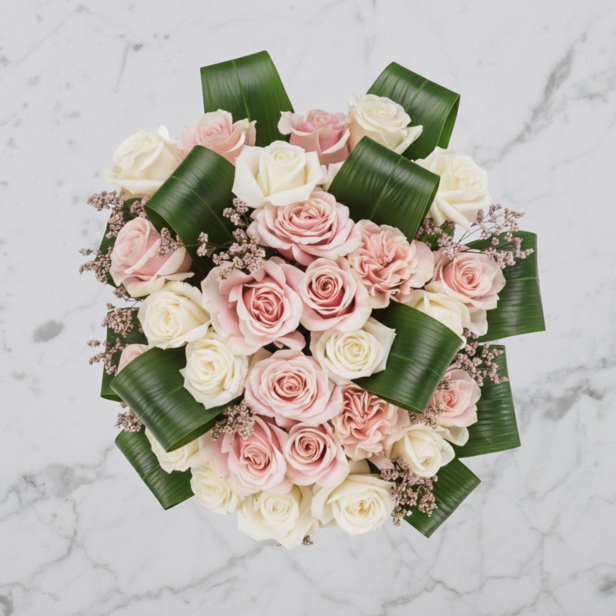 Round bouquet of soft pink and white roses with folded dark green leaves