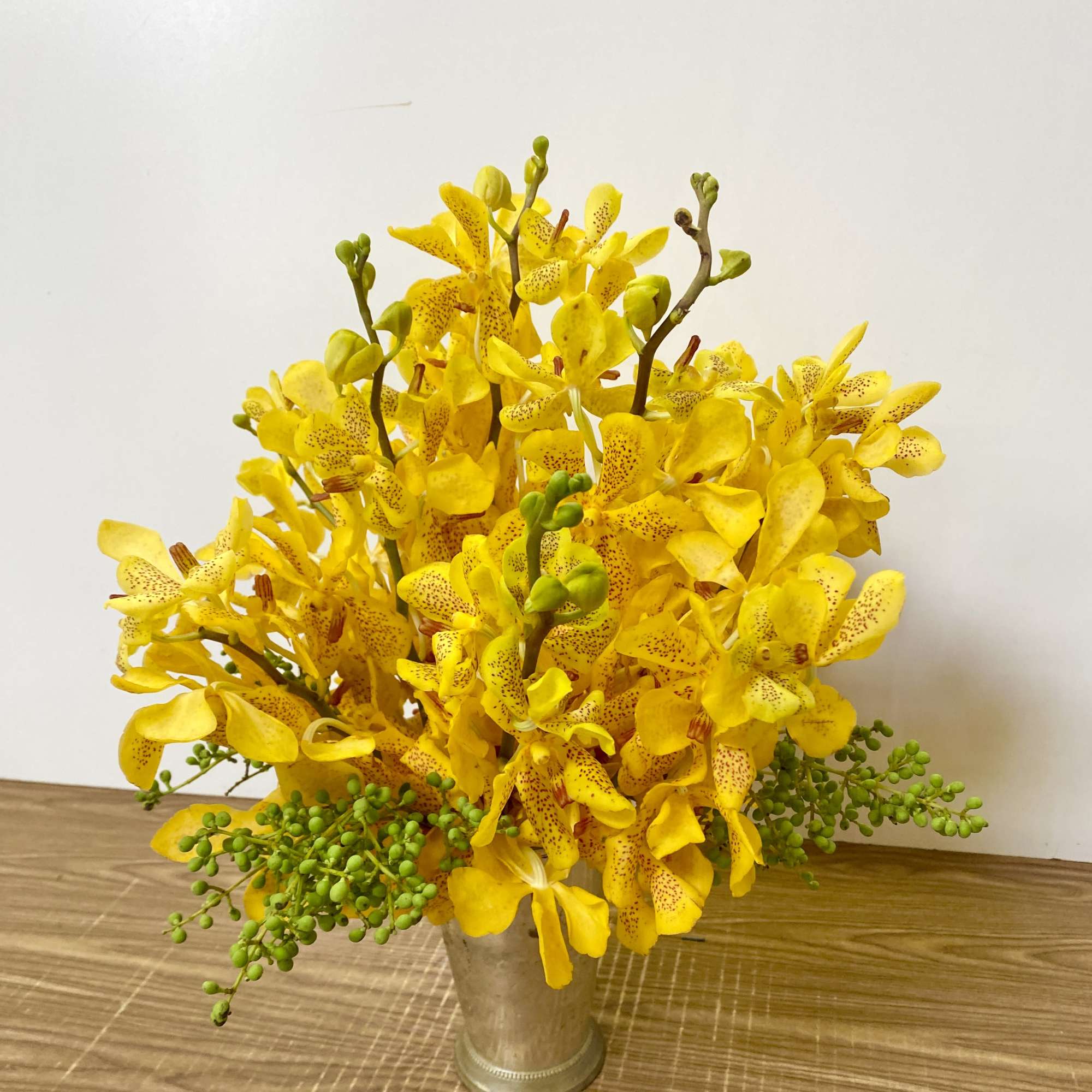Yellow orchid arrangement in a metal vase with green berry accents