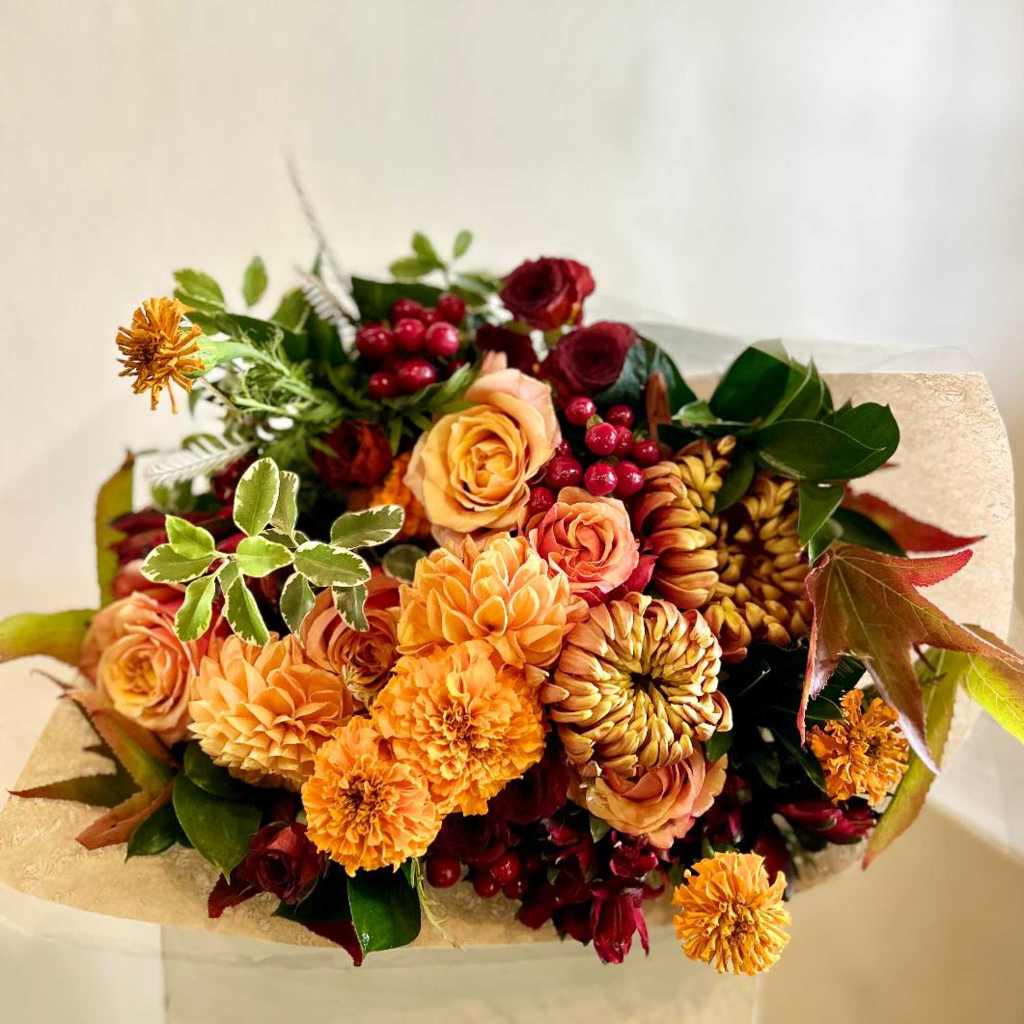 Bouquet of orange and burgundy flowers with berries and greenery wrapped in paper