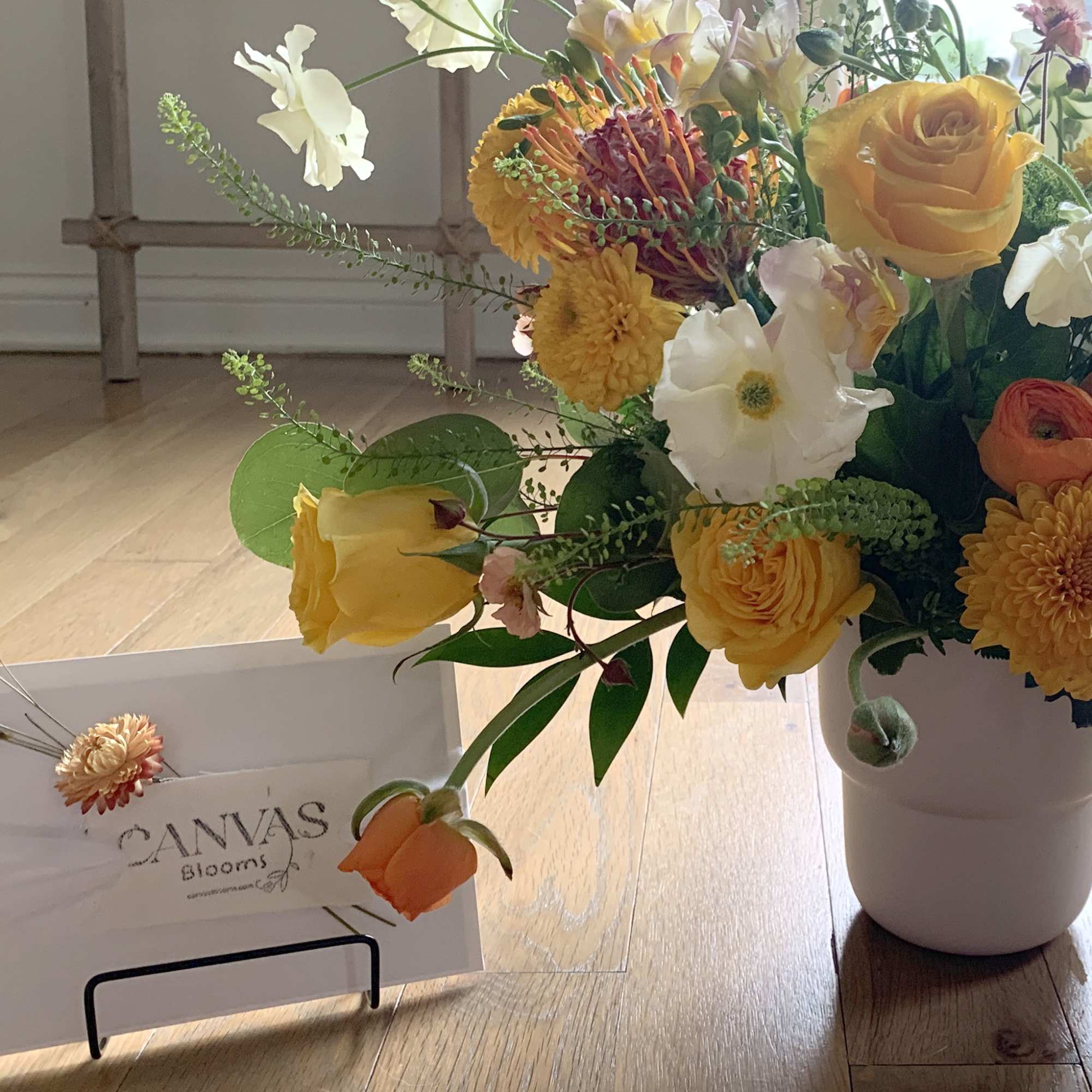 Yellow and white floral arrangement in a white vase with a card holder