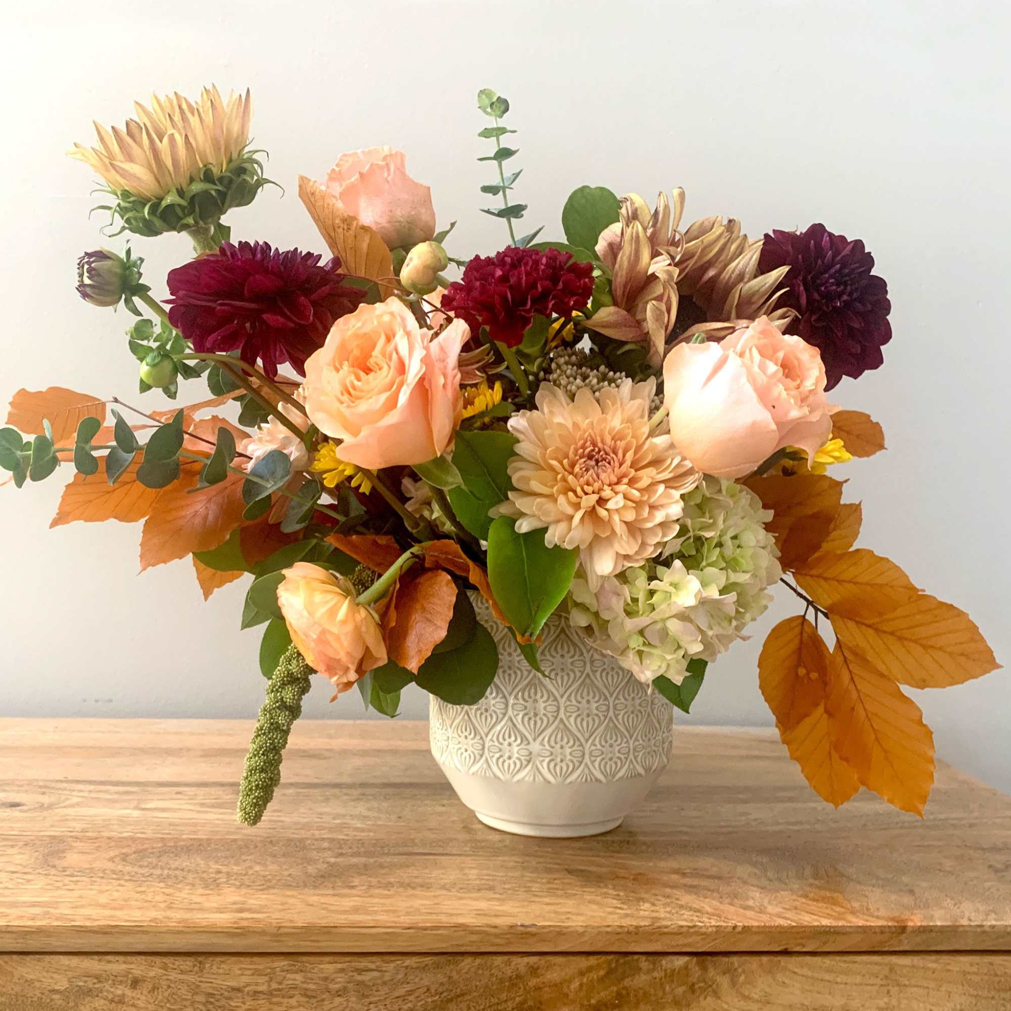 Mixed bouquet of peach, burgundy, and cream flowers in a white vase