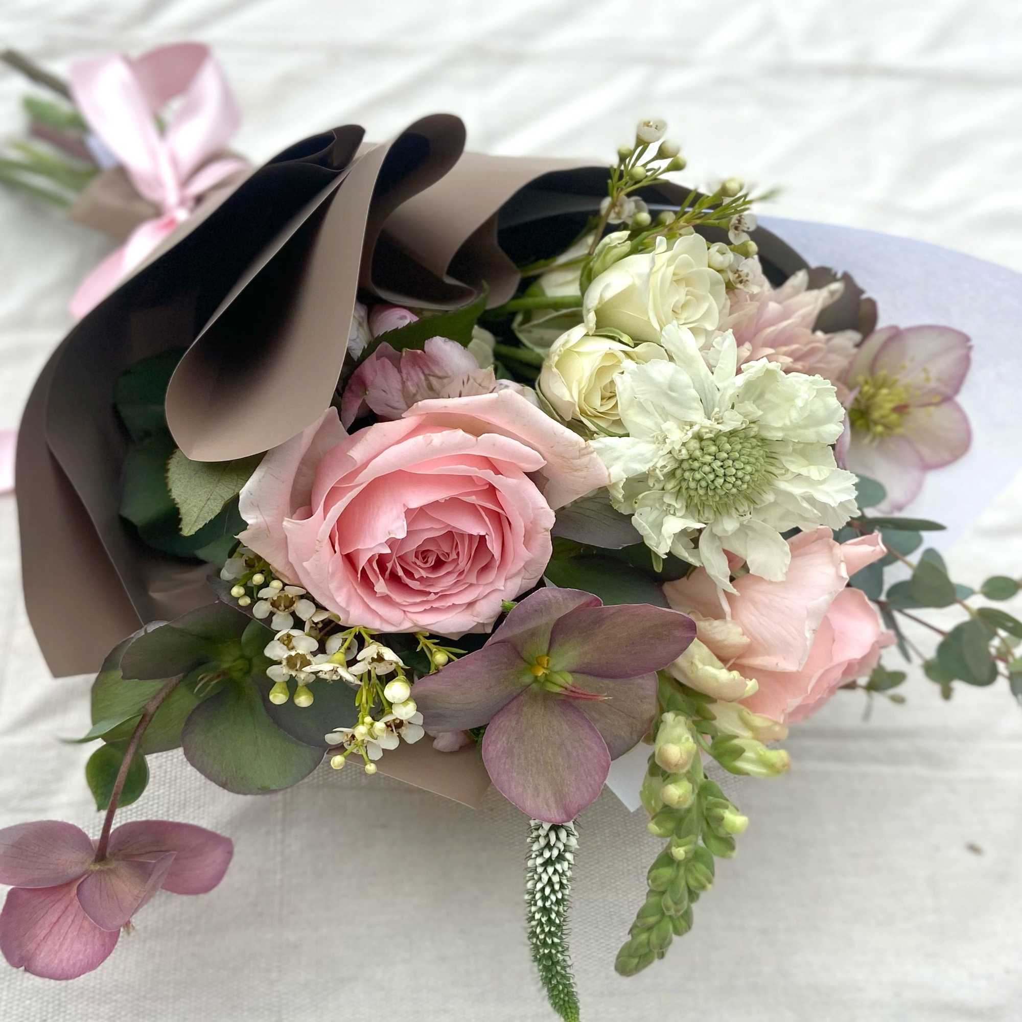 Pink and white bouquet wrapped in brown paper with a ribbon