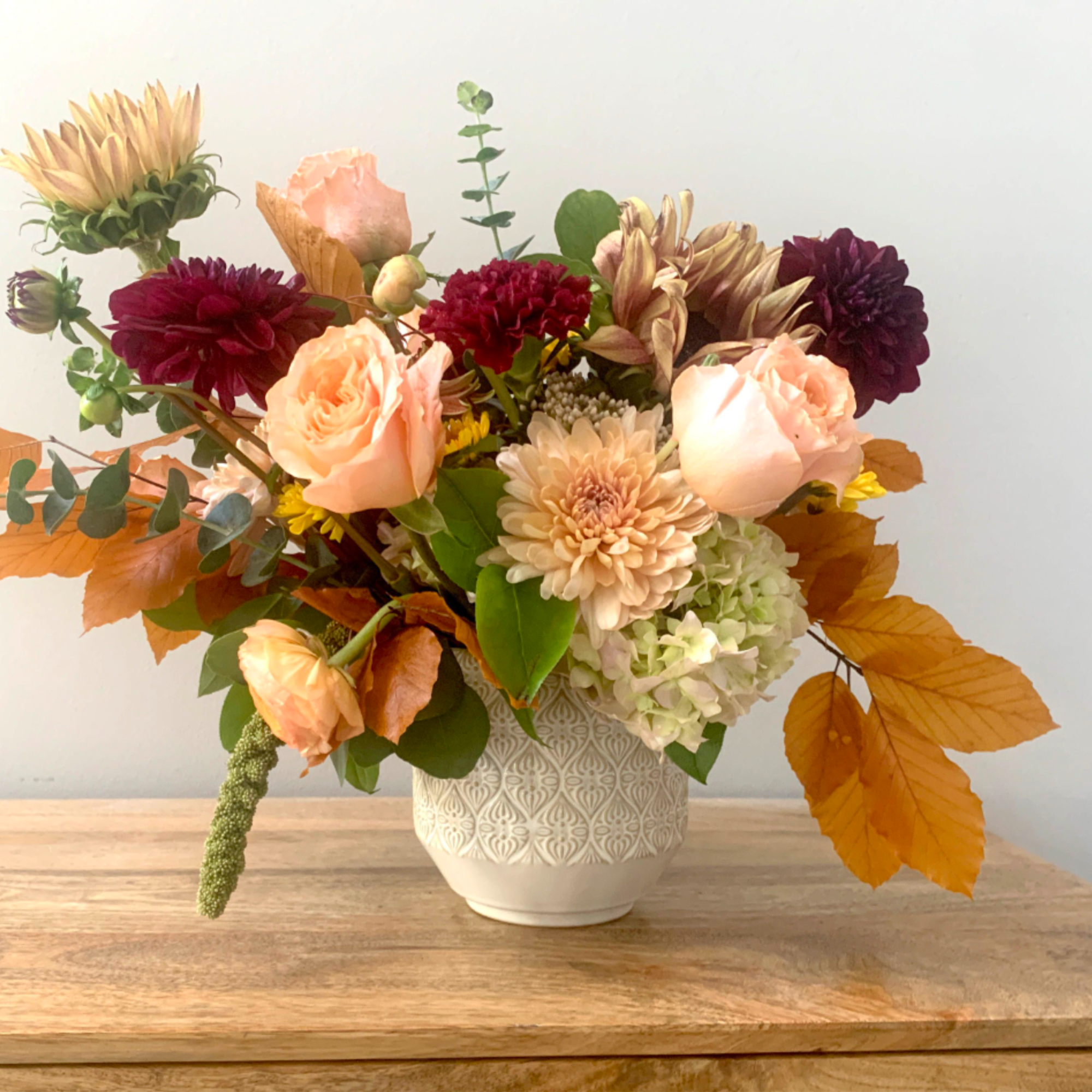 Mixed bouquet of peach, burgundy, and cream flowers in a white vase