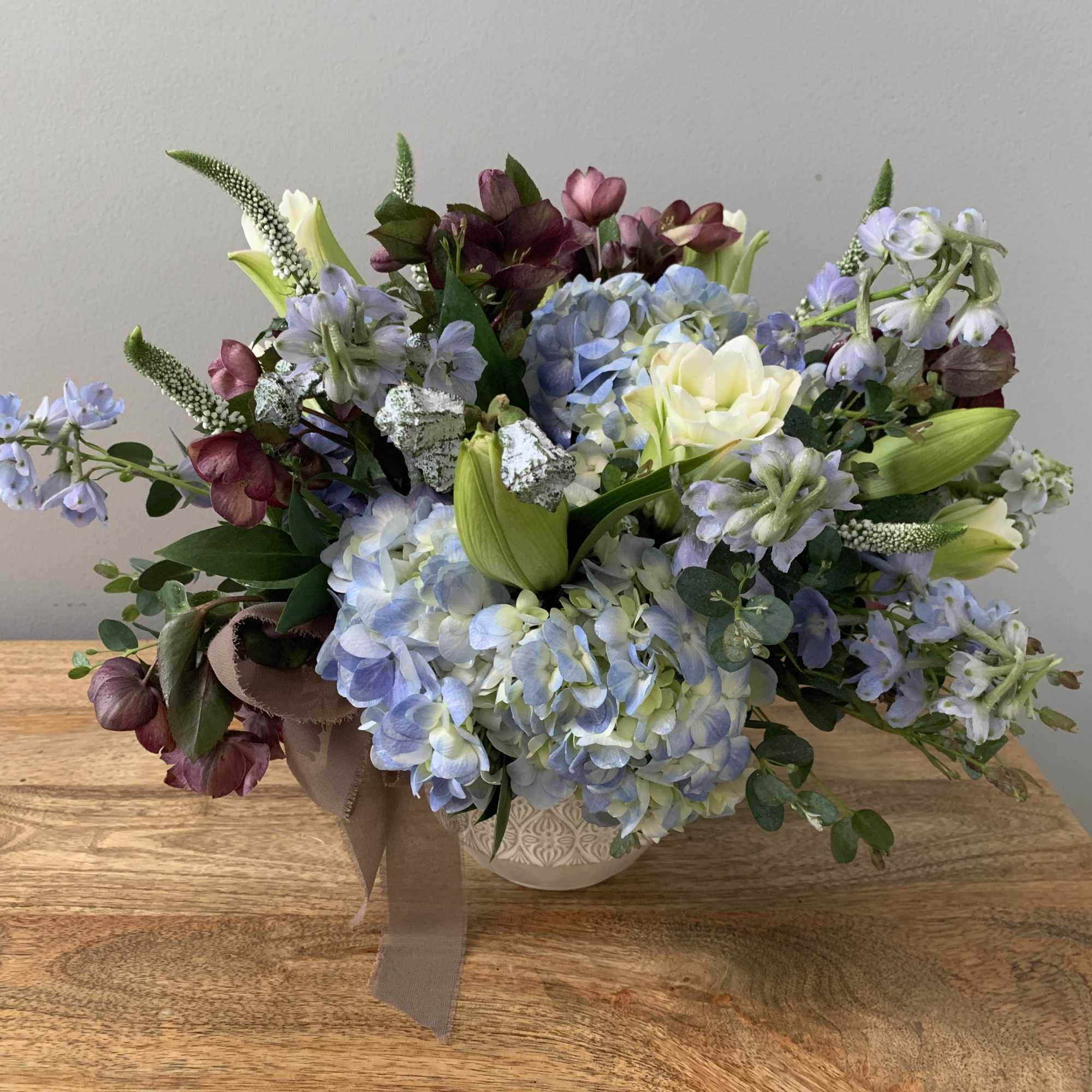 Mixed bouquet of blue hydrangeas, lilies, and purple flowers in a vase