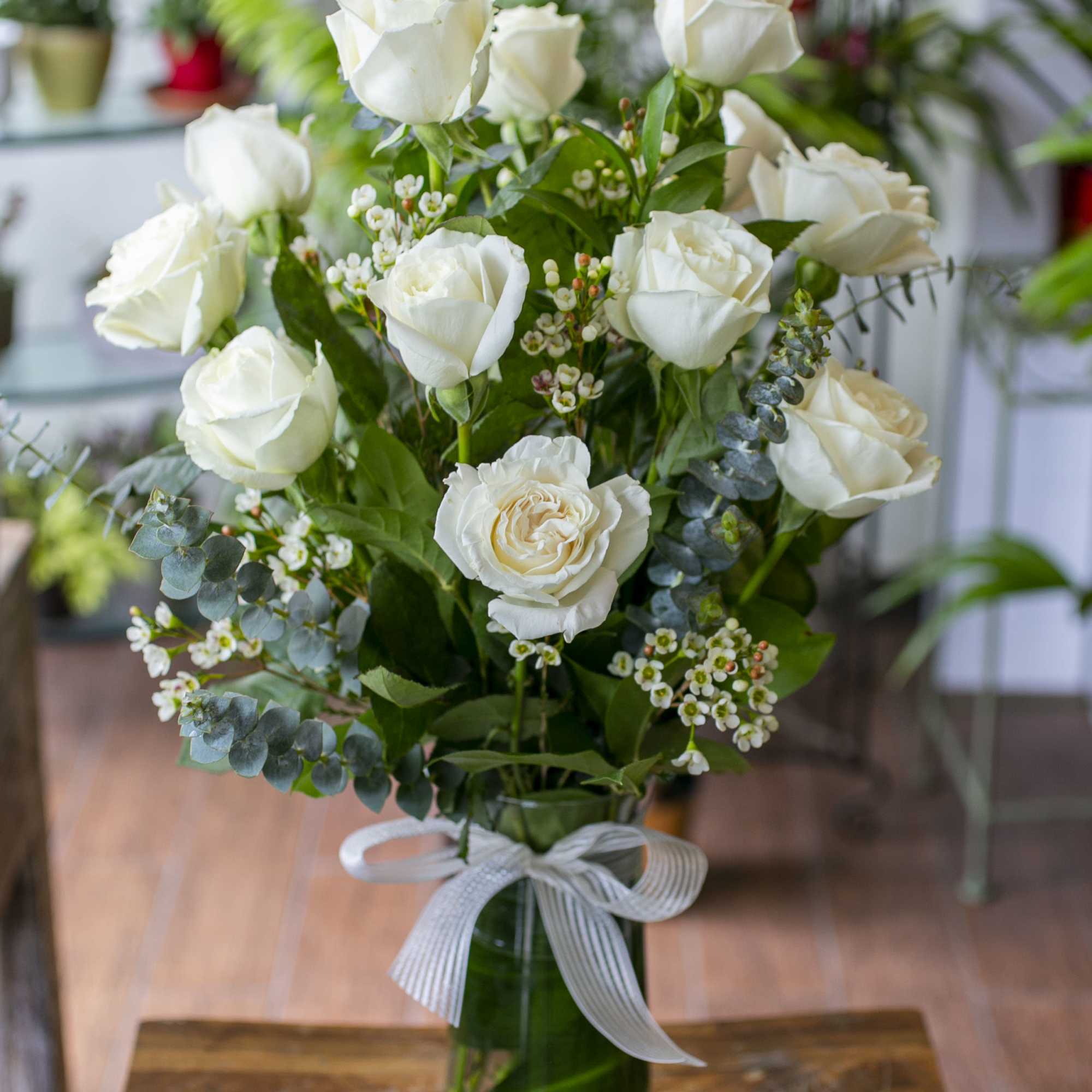 White rose bouquet in a clear glass vase with a ribbon bow