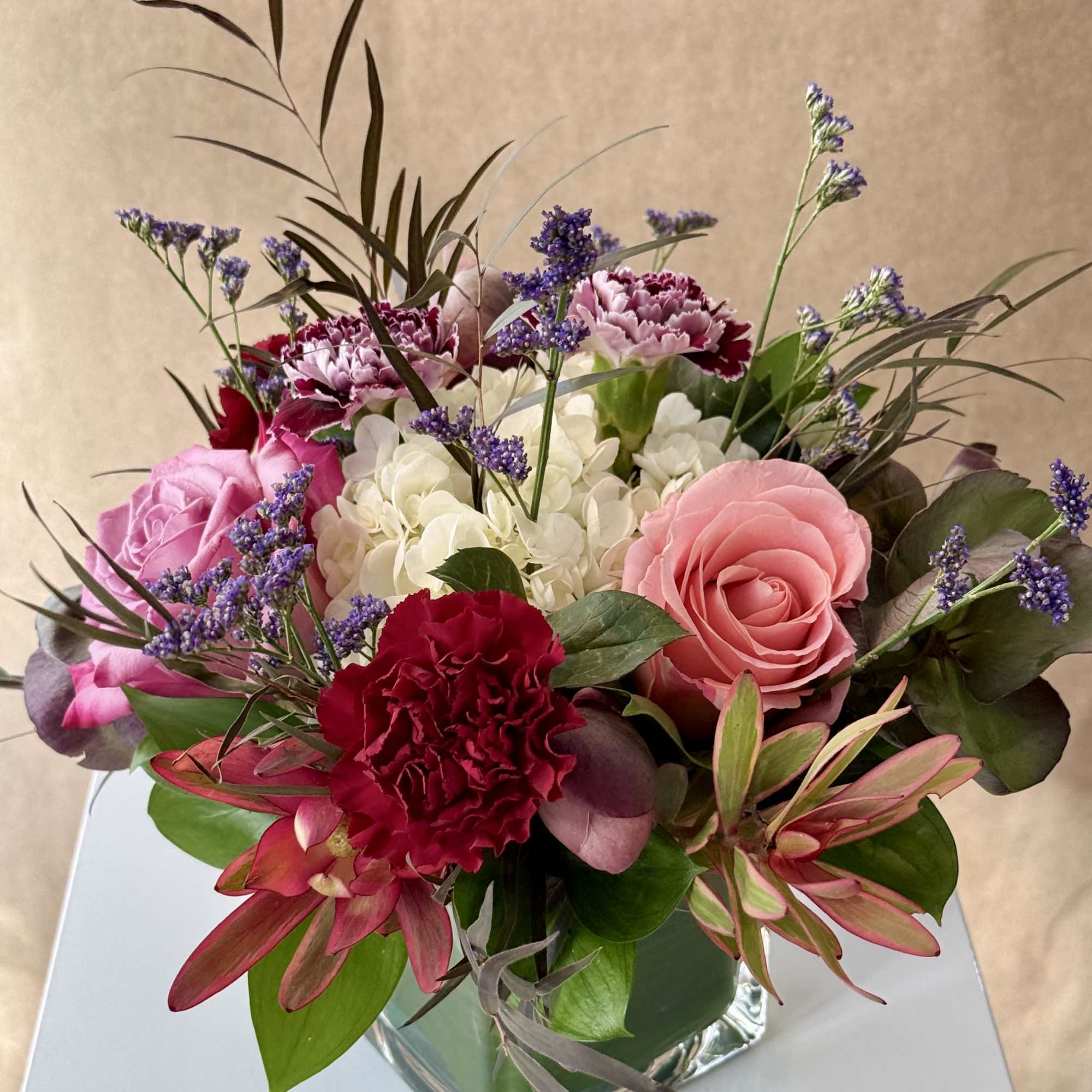 Mixed bouquet of pink roses, carnations, and white hydrangeas in a glass vase