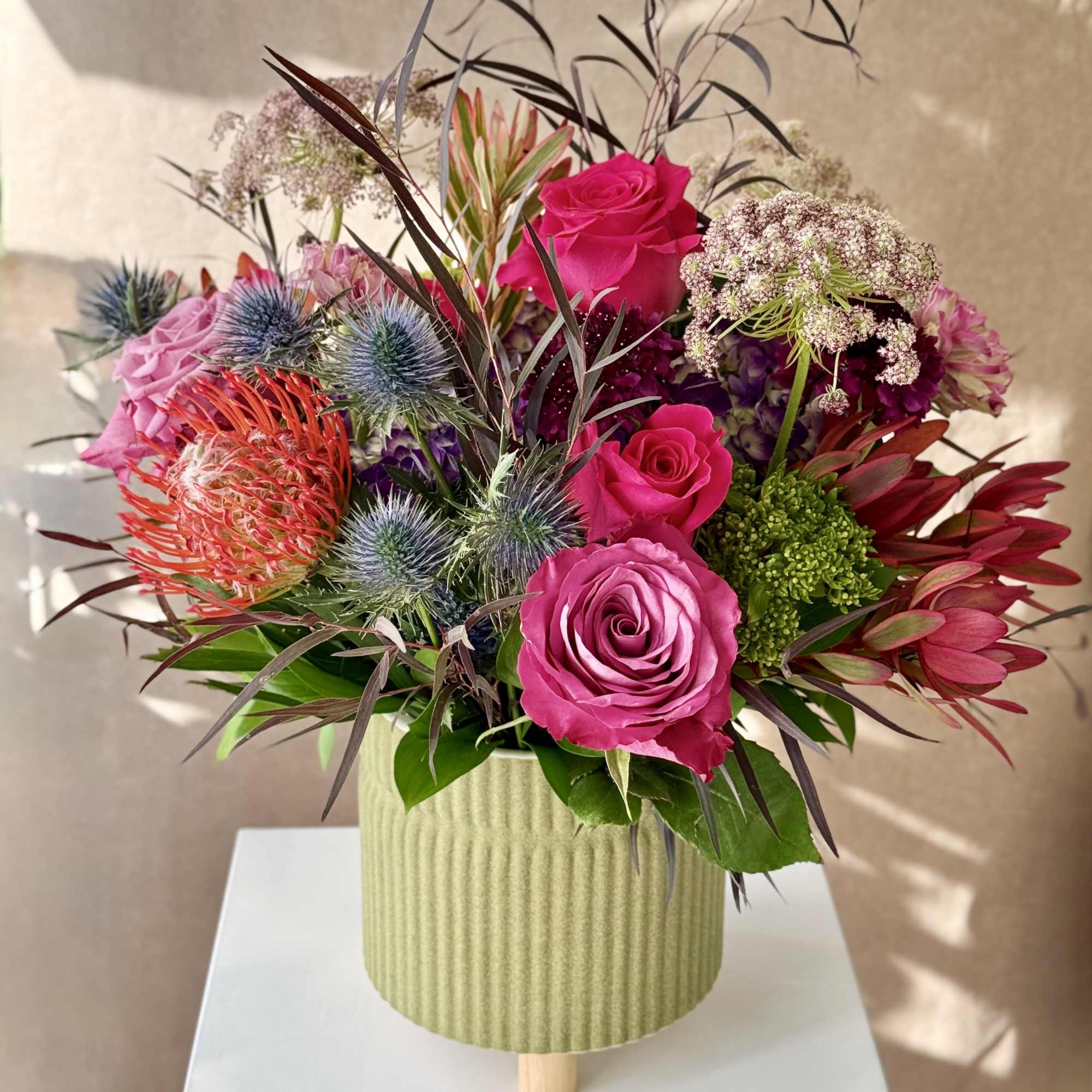 Bouquet of pink roses and spiky flowers in a ribbed green vase