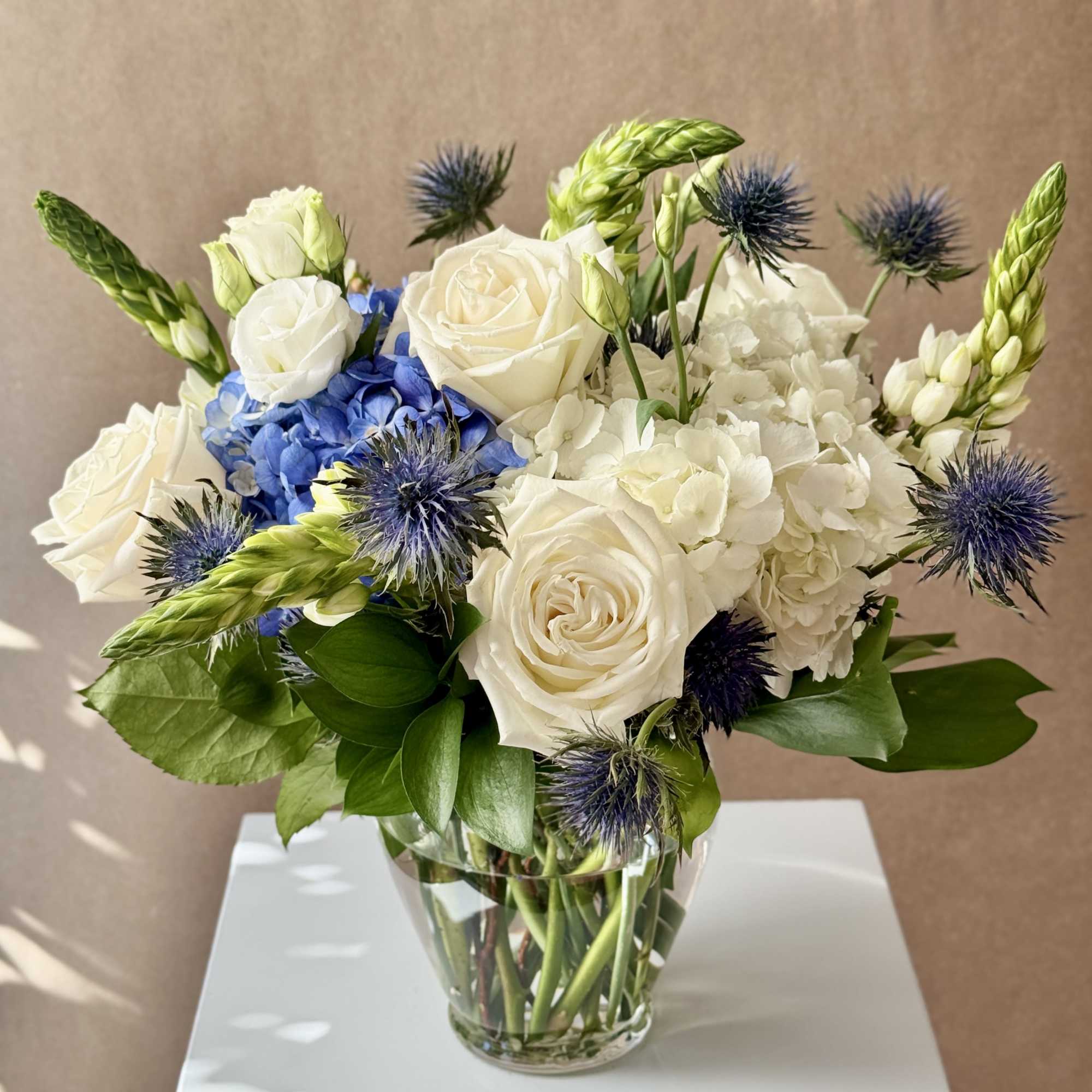 White roses and blue hydrangea in a glass vase with spiky blue thistles