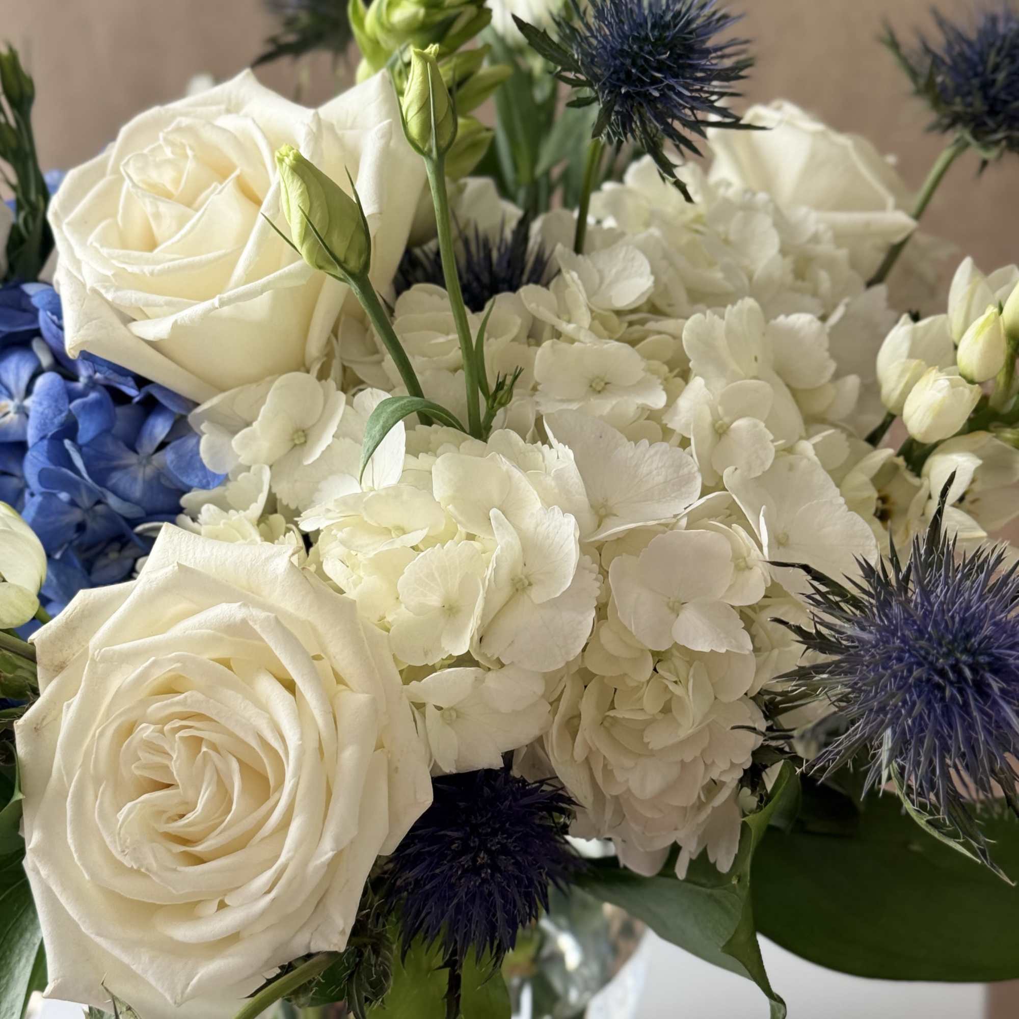 White roses and hydrangeas with blue thistle in a glass vase