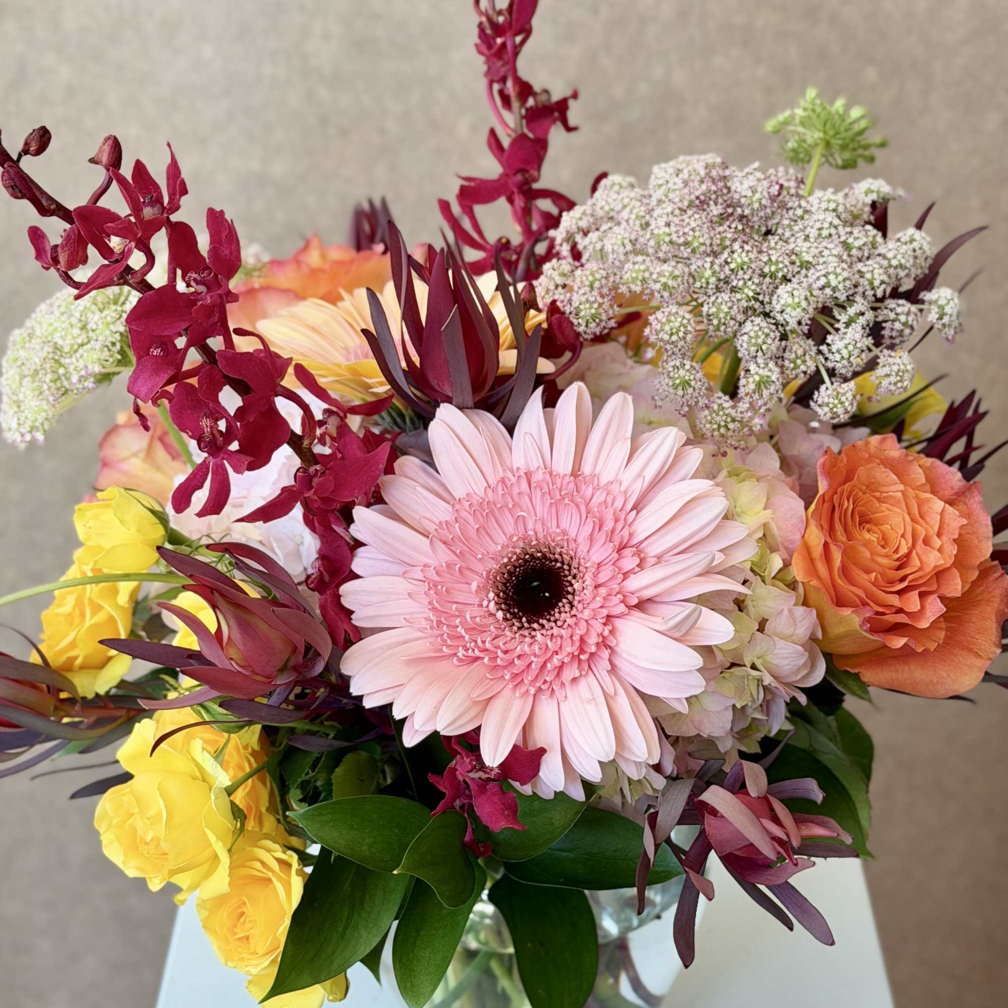 Mixed bouquet with a pink gerbera daisy, roses, and orchids in a glass vase