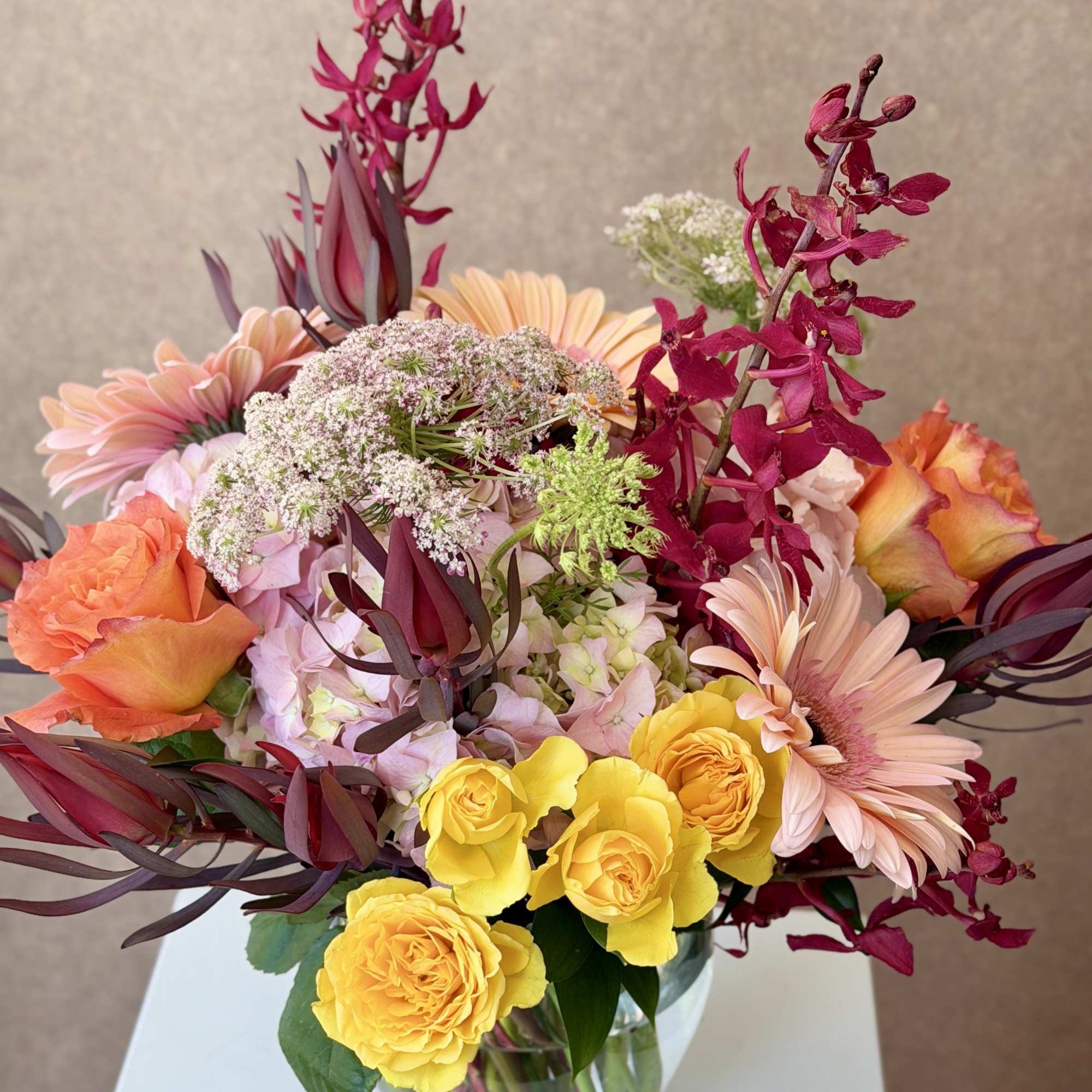 Mixed bouquet of yellow and peach roses with pink daisies in a glass vase