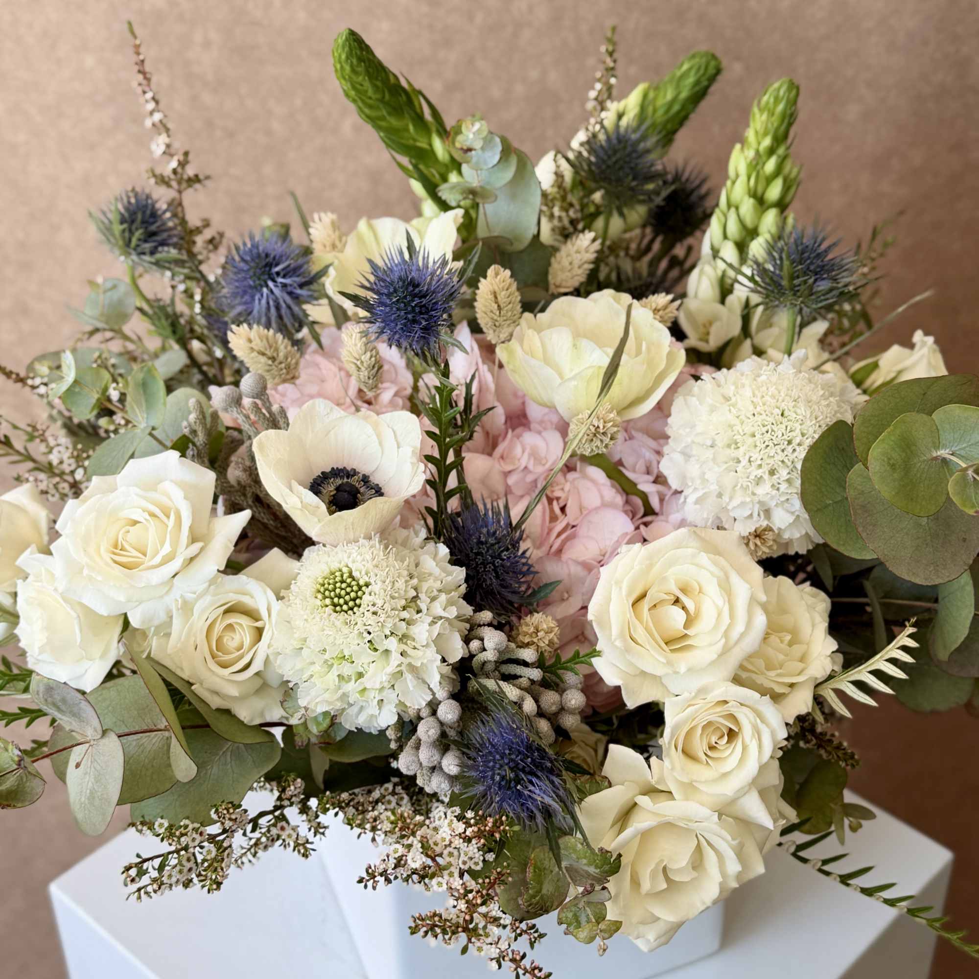 Bouquet of cream roses, pale pink blooms, and blue thistles in a white box