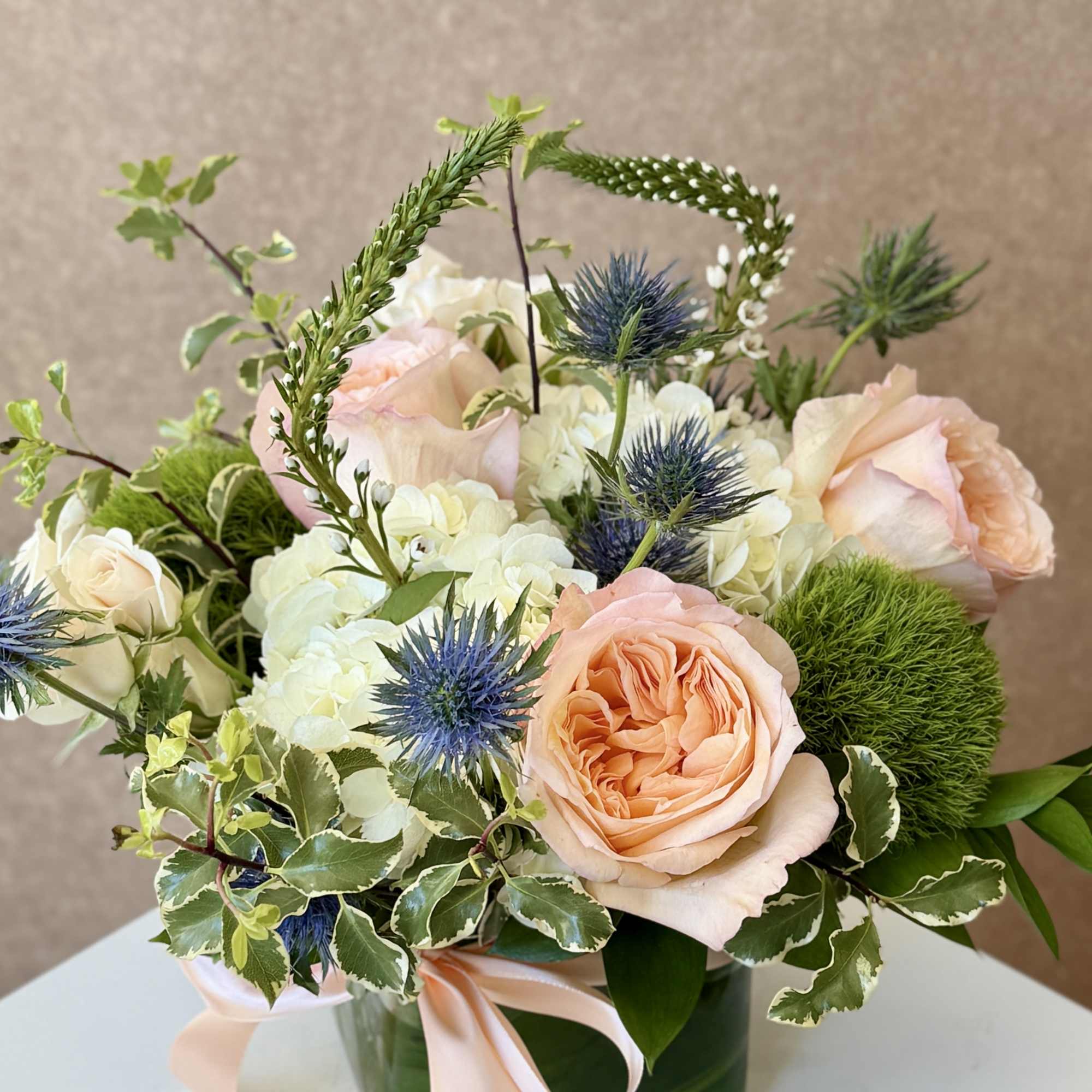 Peach roses and white hydrangeas in a green glass vase with a pink ribbon