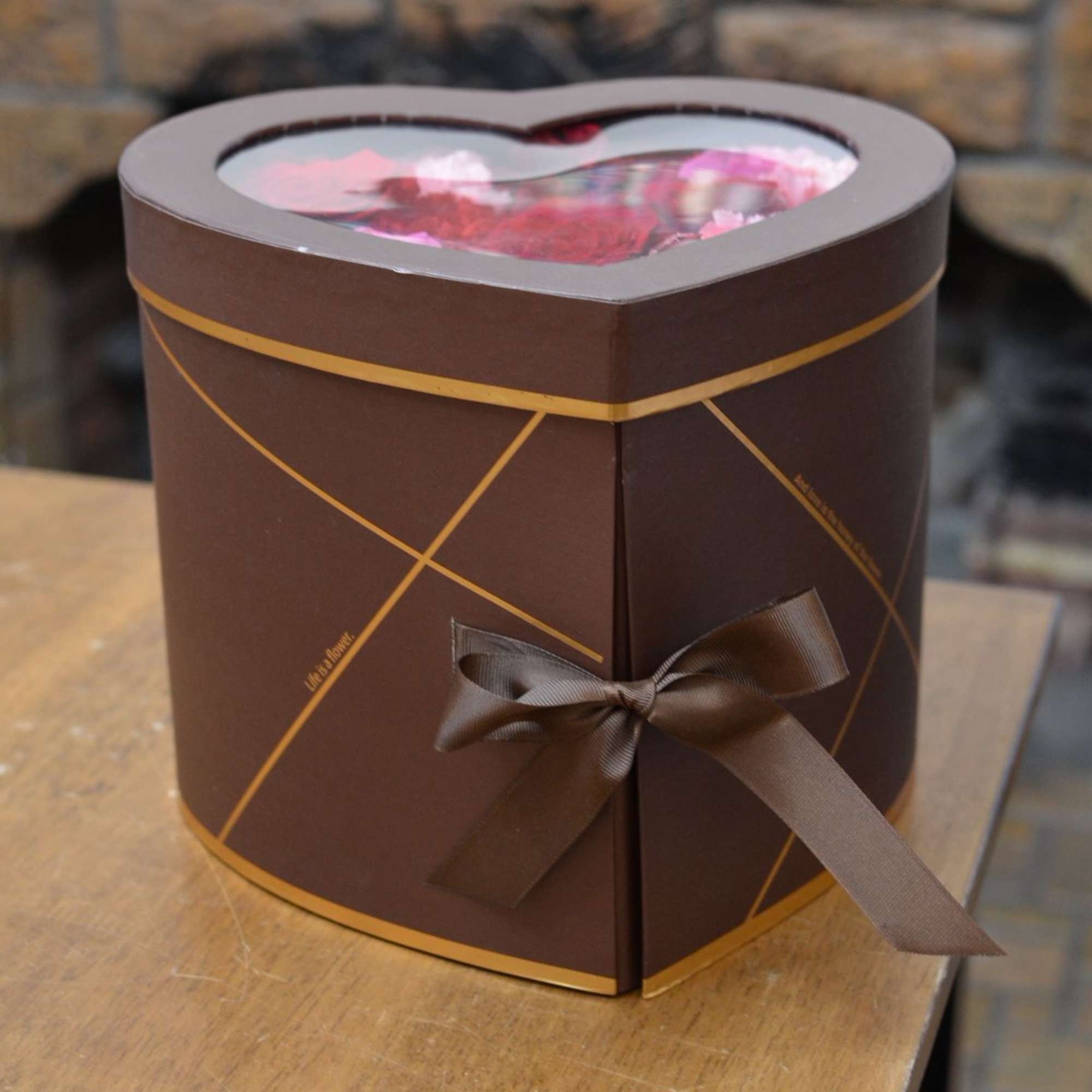 Heart-shaped gift box with pink flowers inside and a brown ribbon