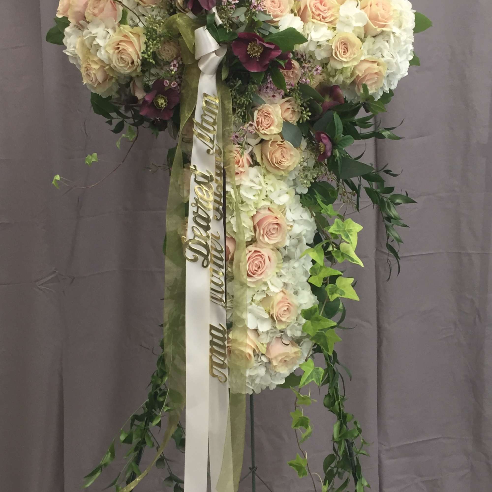 Standing floral cross with pale roses and white blooms on a metal easel
