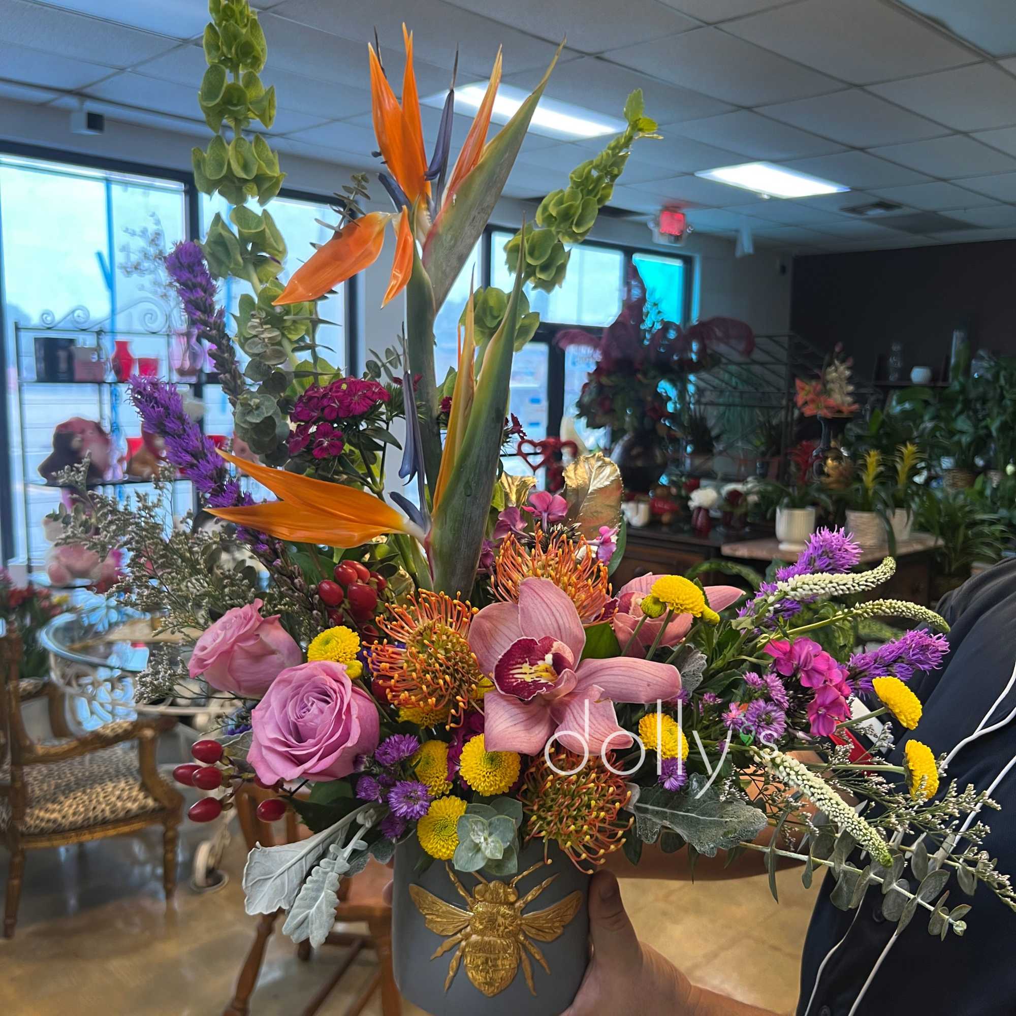 Colorful mixed flower arrangement in a gray vase with a gold bee