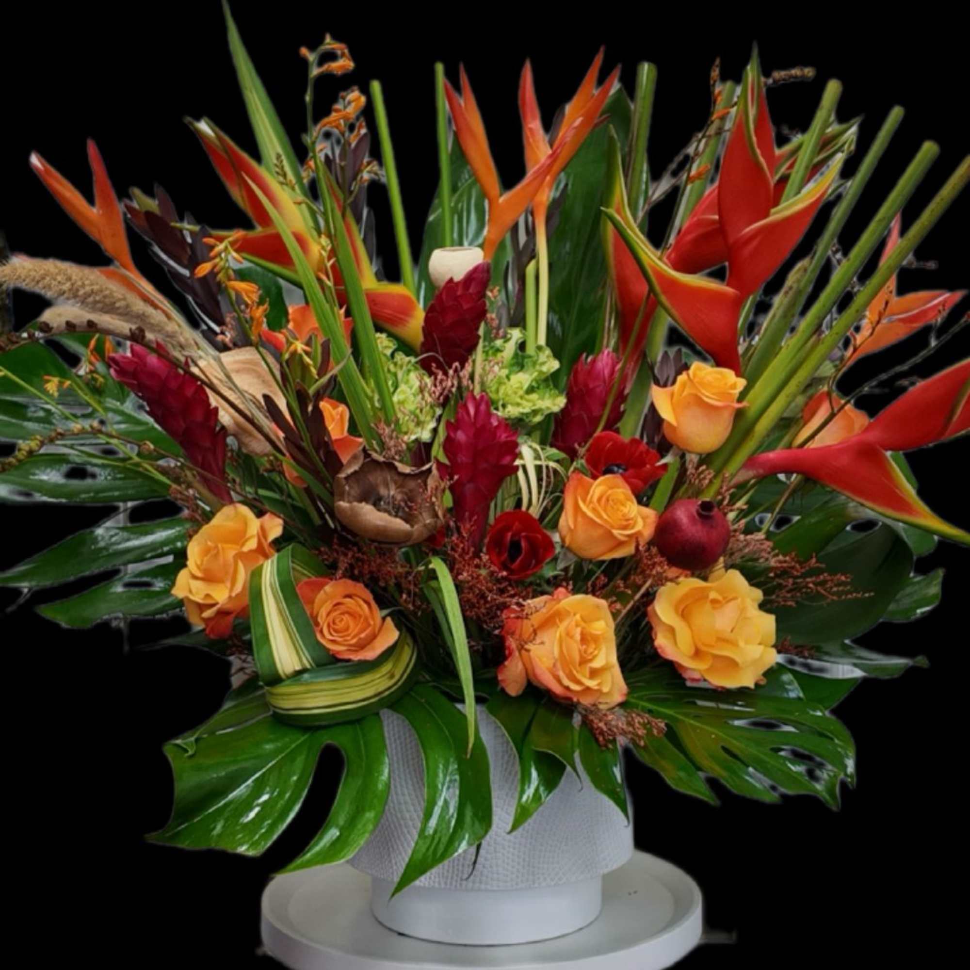 Tropical floral arrangement with orange roses and red heliconia in a white vase