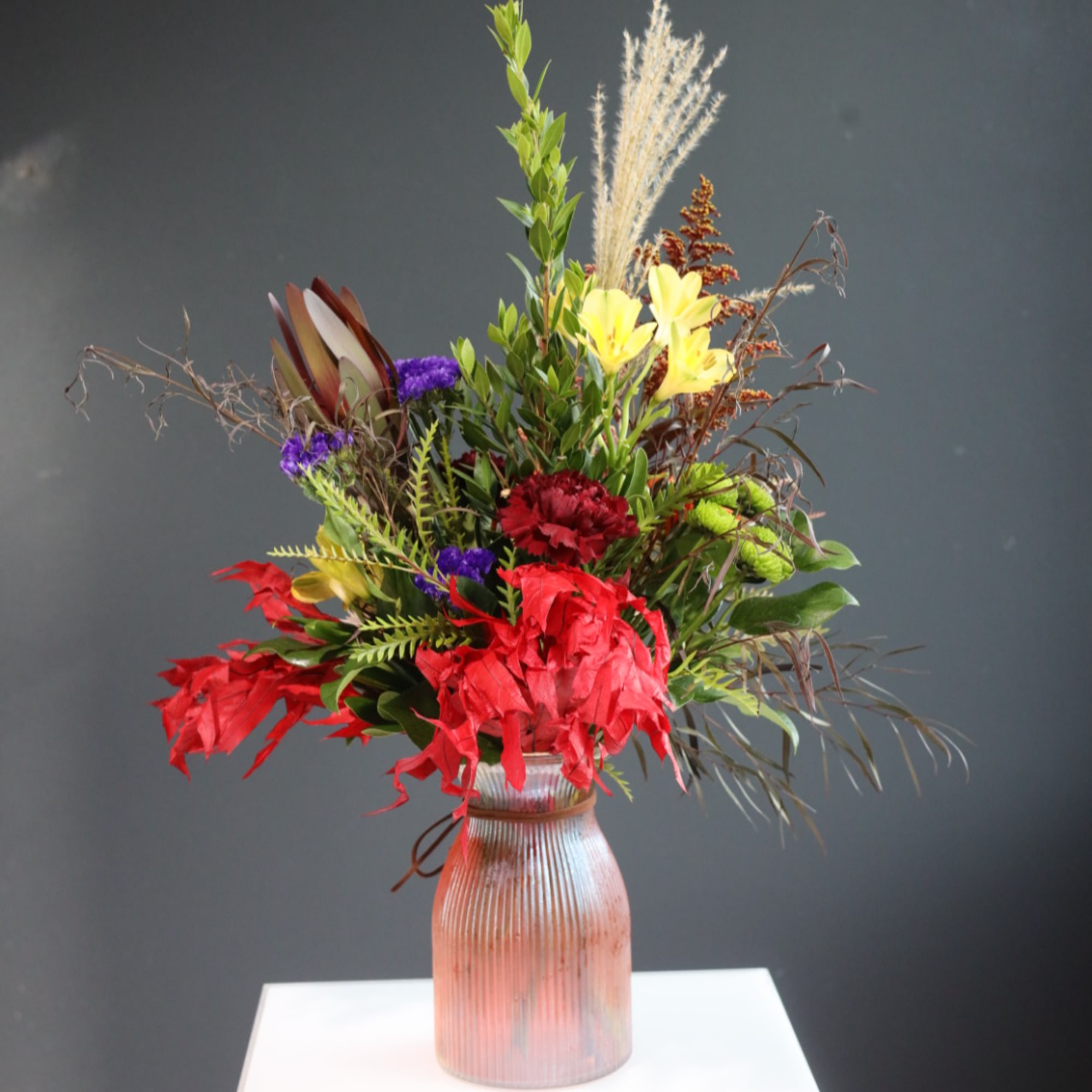 Tall mixed bouquet in a ribbed glass vase with red, yellow, and purple flowers