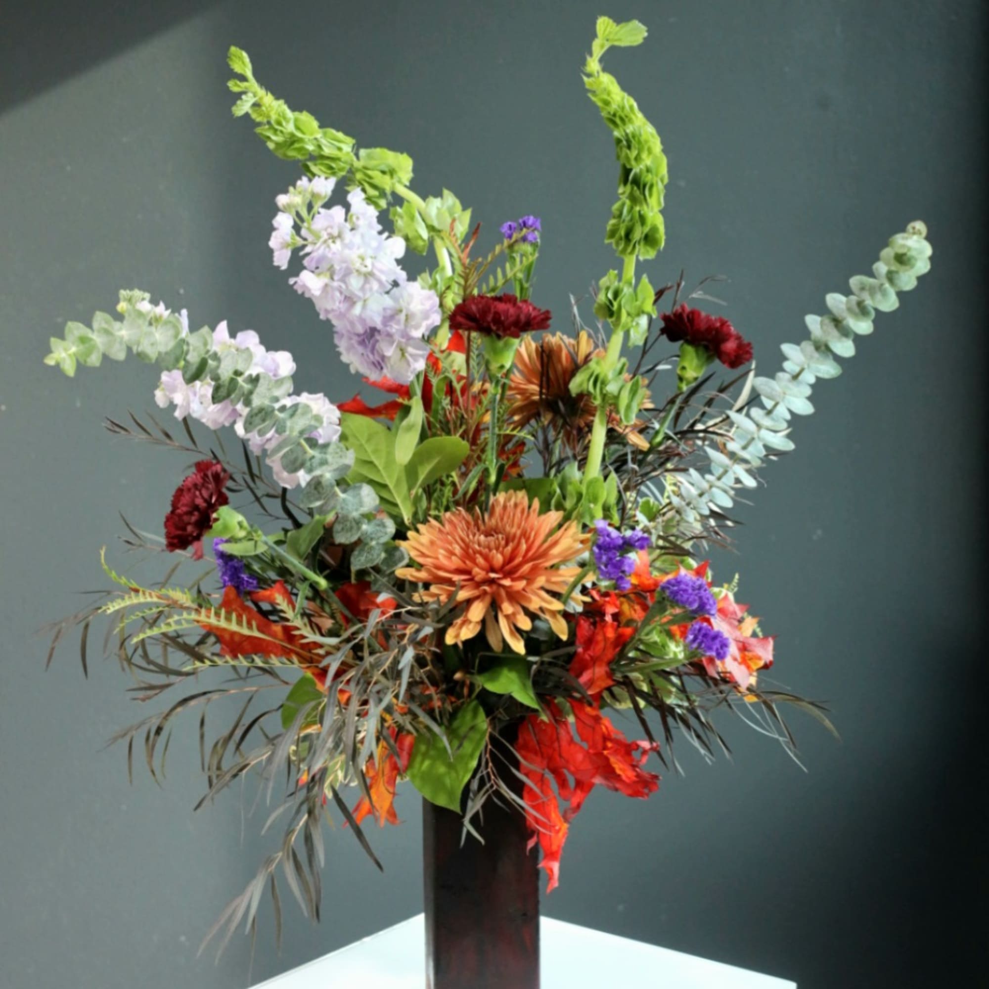 Tall mixed floral arrangement in a dark vase with orange and purple blooms