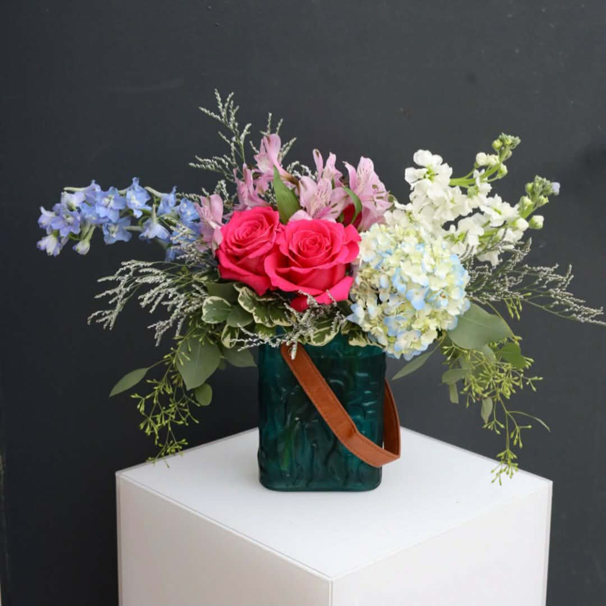 Mixed bouquet of pink roses, blue and white blooms in a green vase