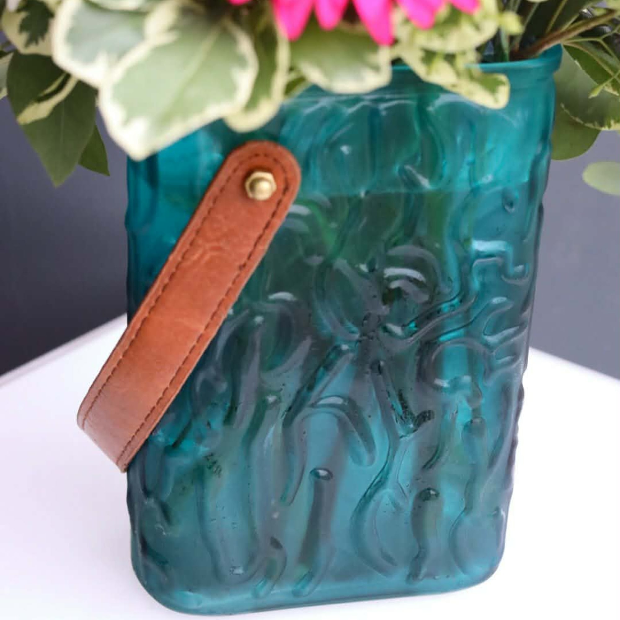 Blue glass vase with flowers and a tan leather handle