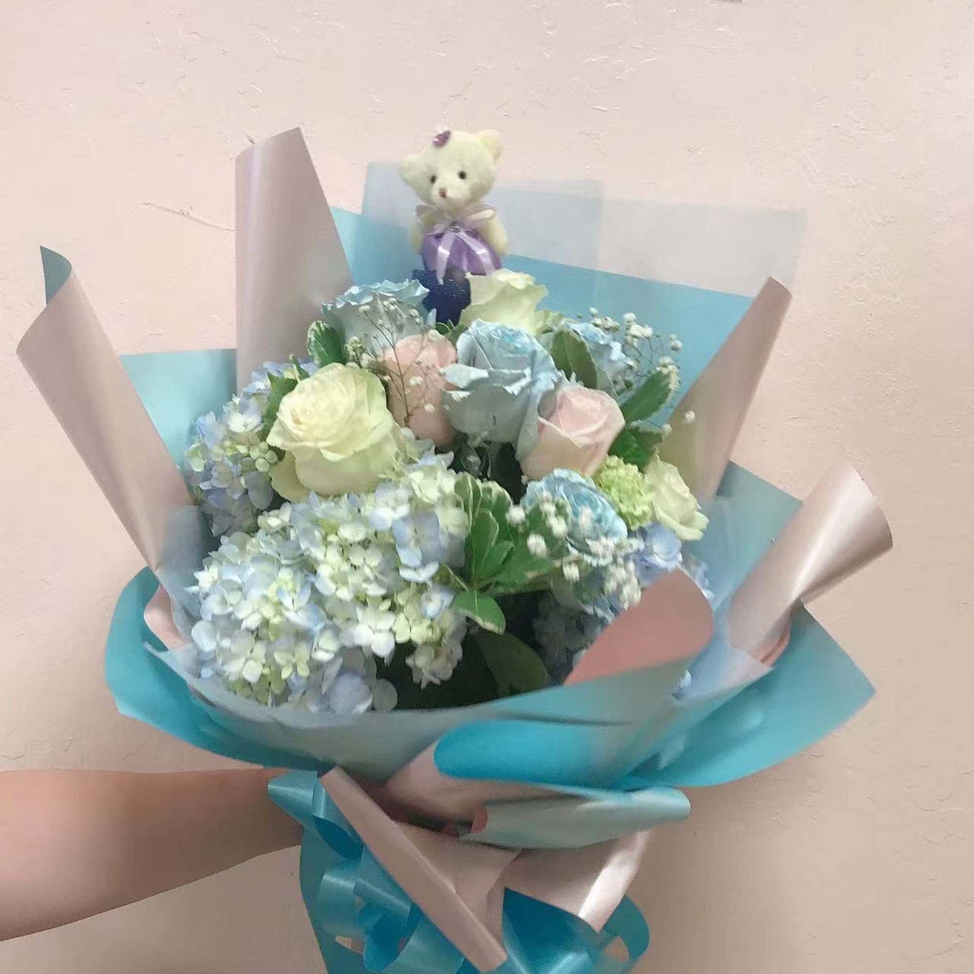 Pastel bouquet with roses and hydrangeas, topped with a small teddy bear