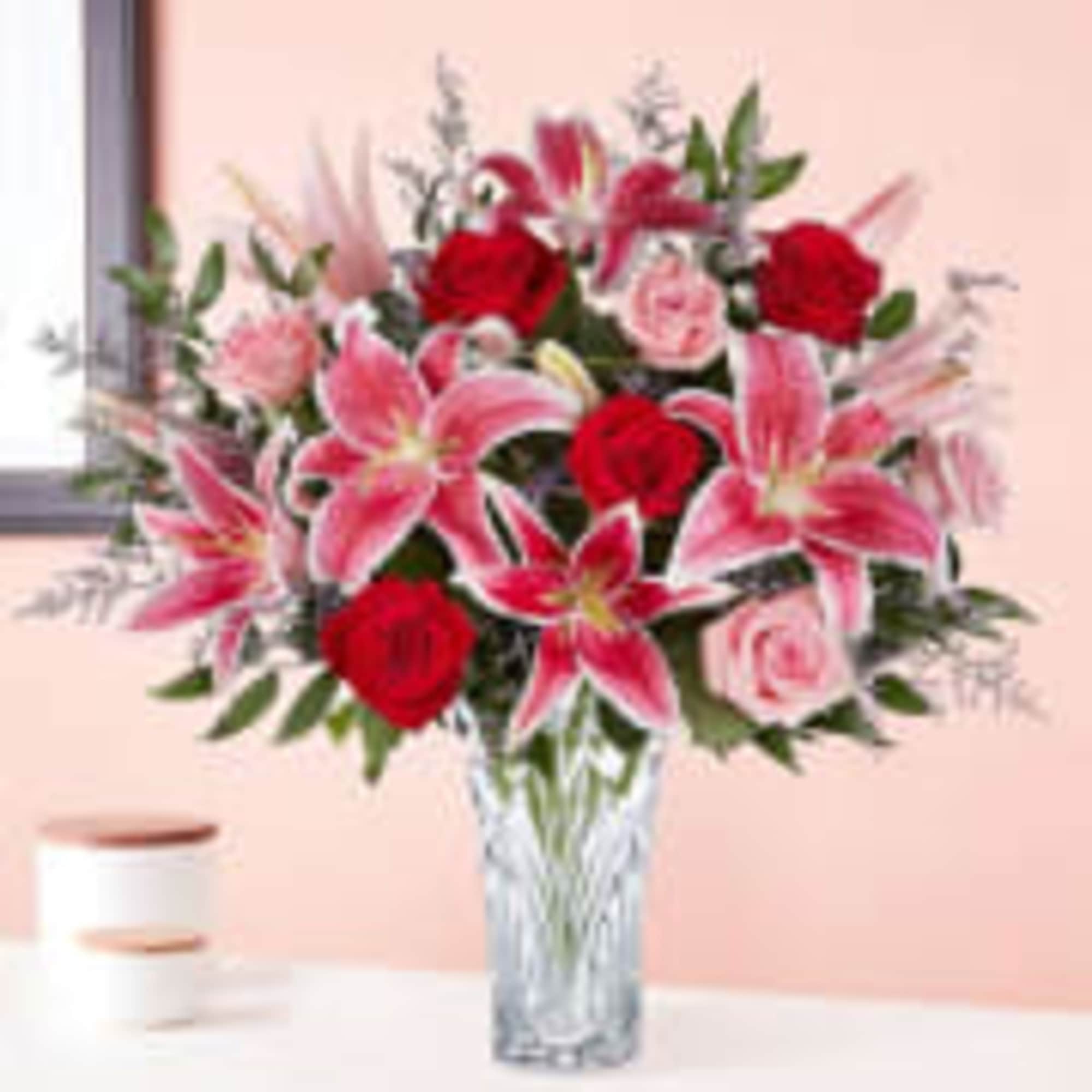 Pink lilies and red roses arranged in a clear glass vase