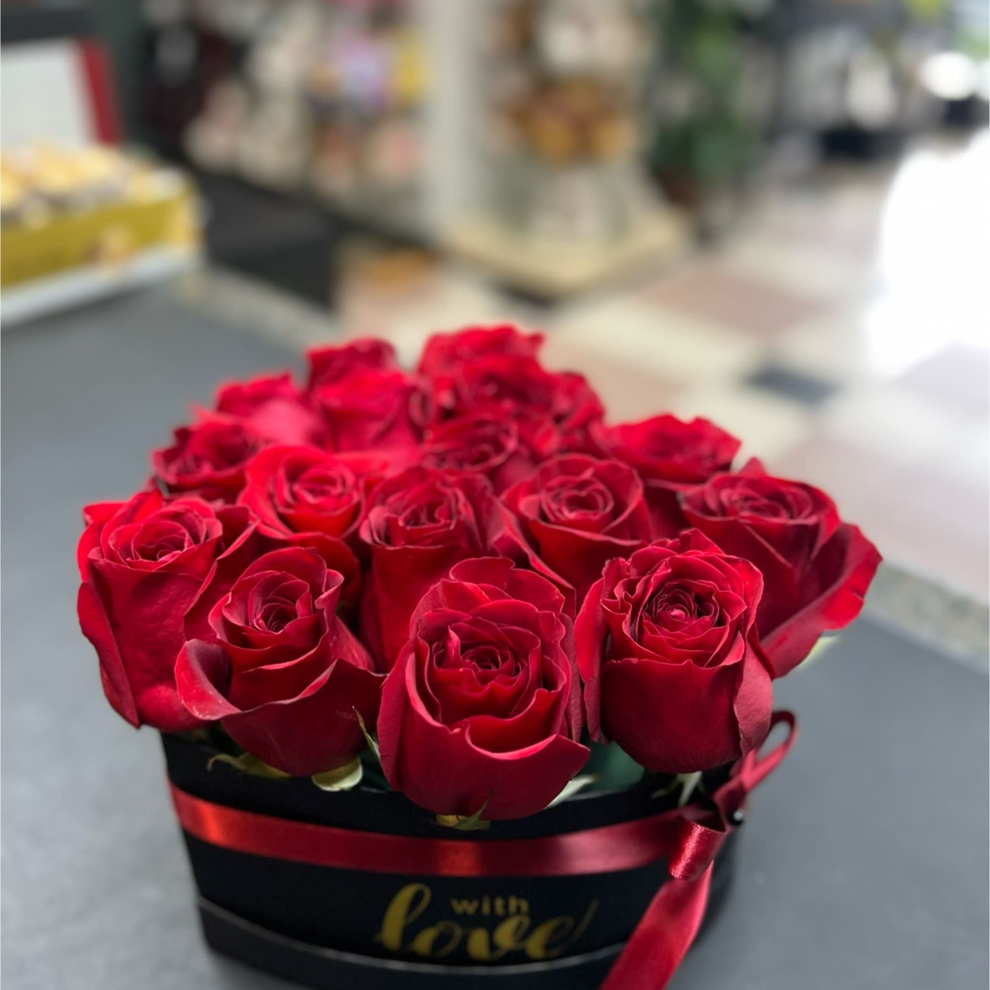 Red roses arranged in a black hat box with a red ribbon