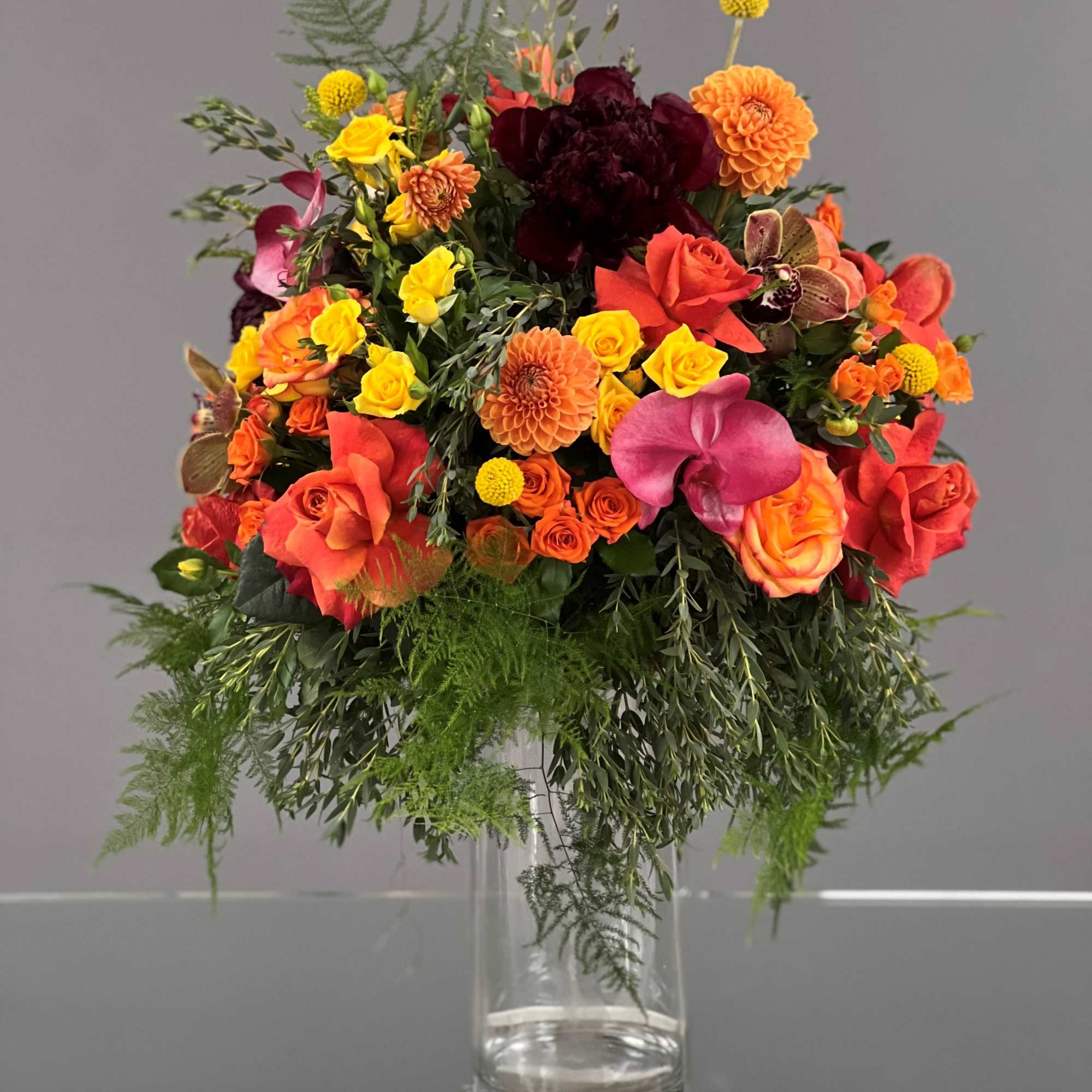 Colorful bouquet of roses, orchids, and dahlias in a clear glass vase