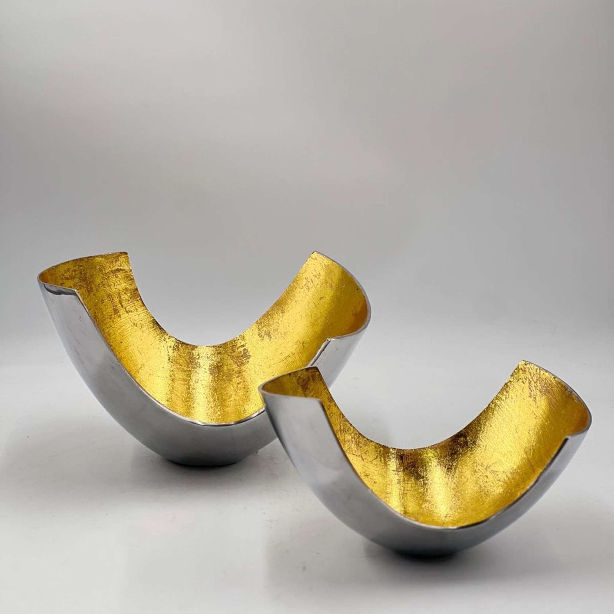 Two metallic gold and silver decorative bowl-shaped objects on a white surface