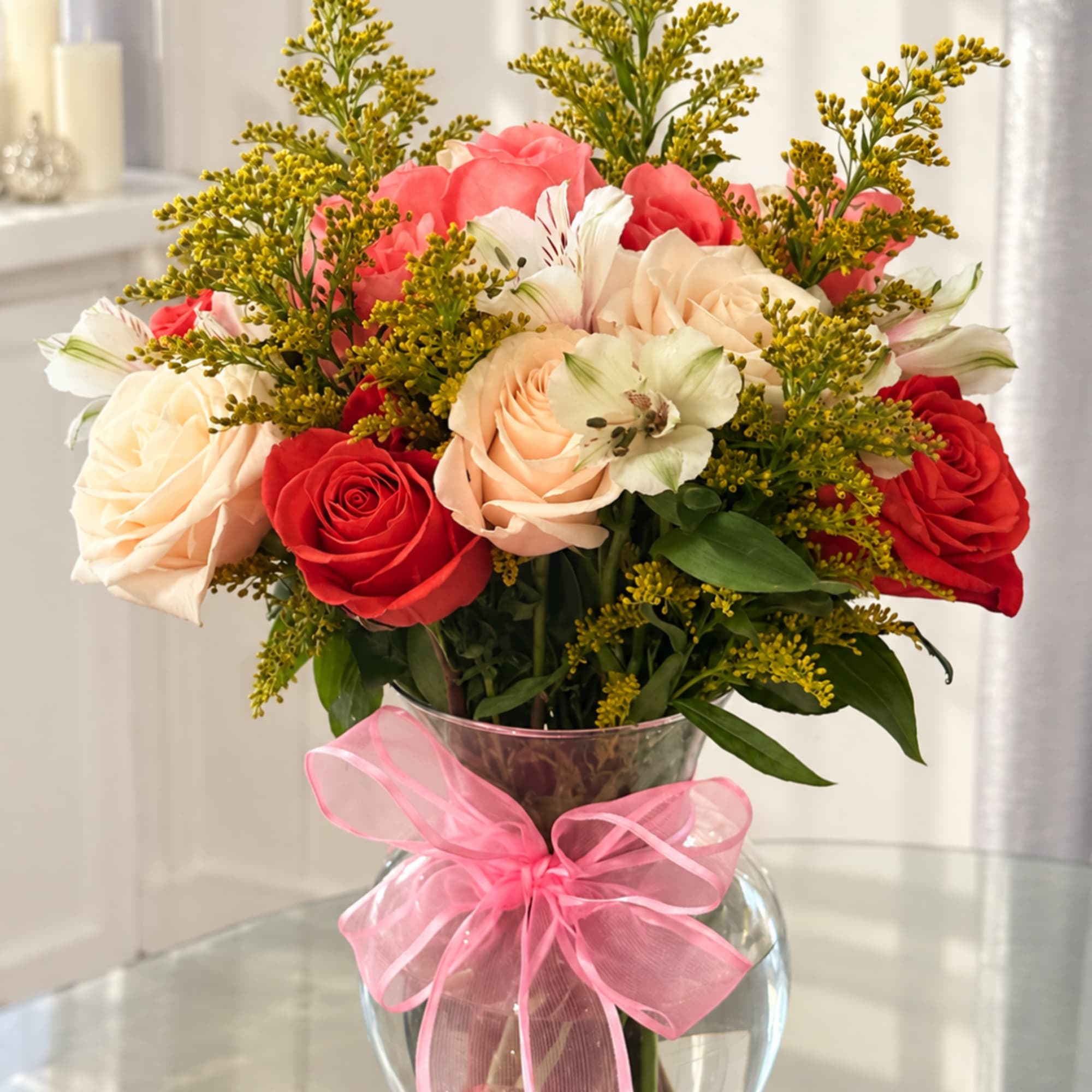 Bouquet of red and blush roses in a glass vase with a pink ribbon