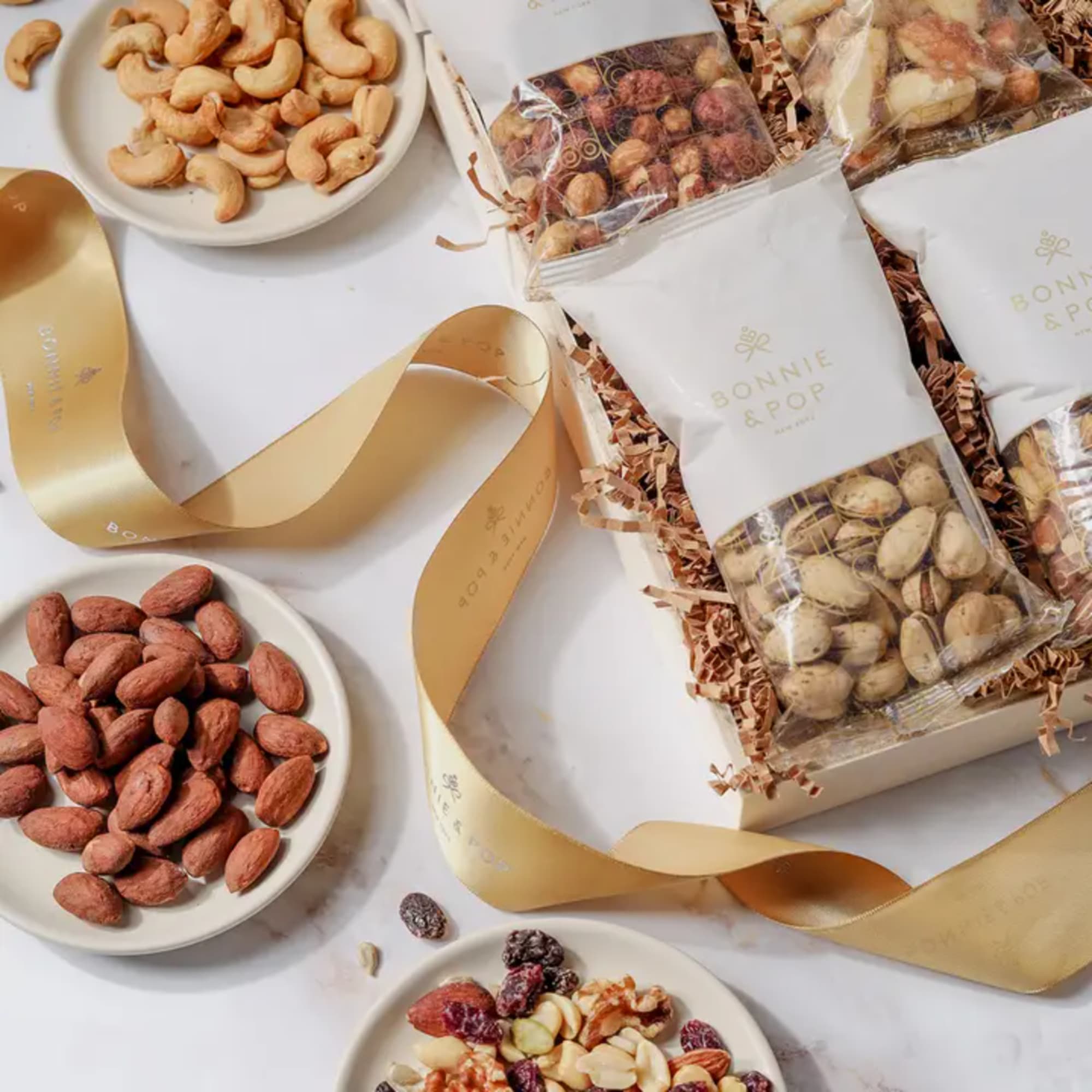 Gift boxes of mixed nuts and dried fruit with gold ribbon on a white surface