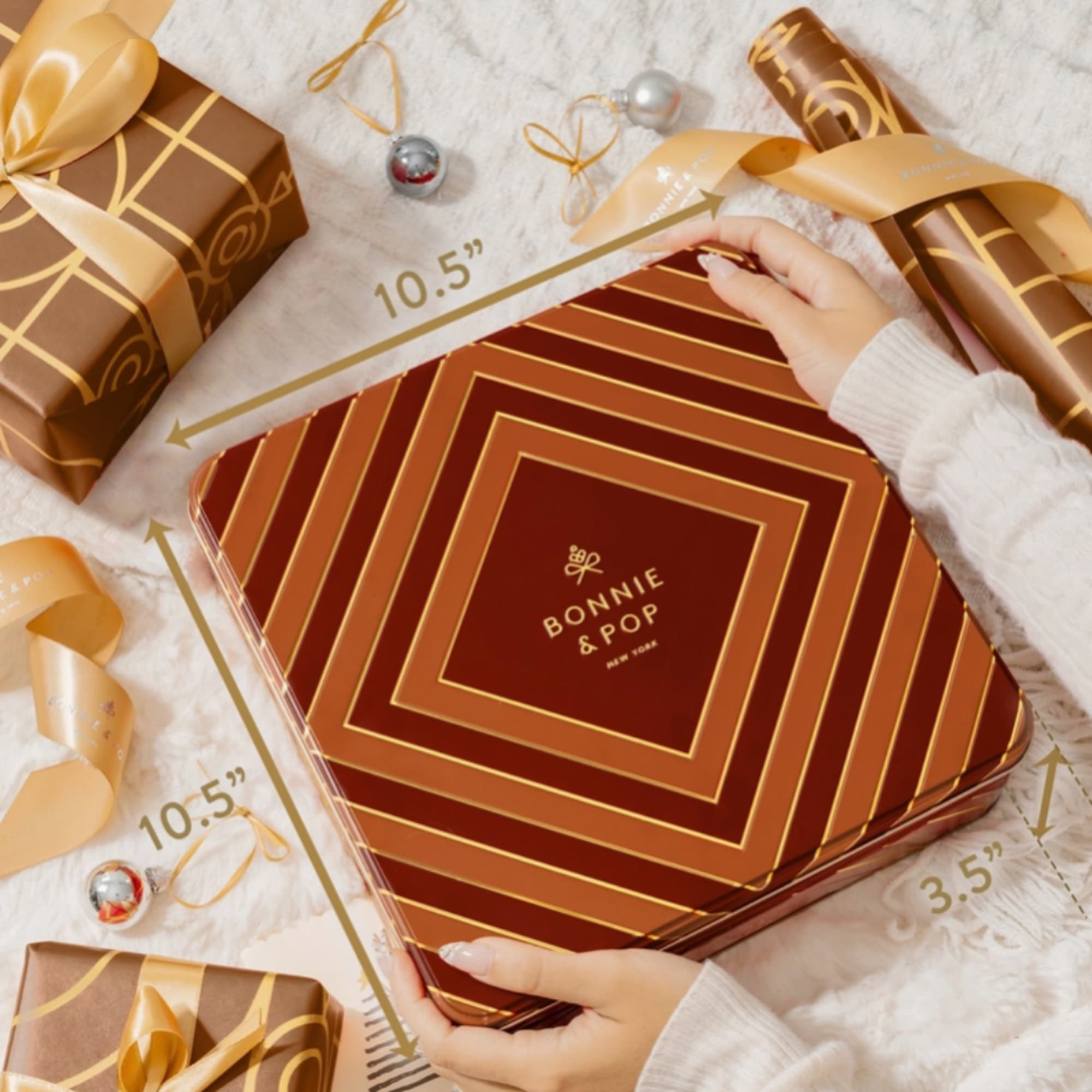 Gift box with gold ribbon and a matching tin held by hands