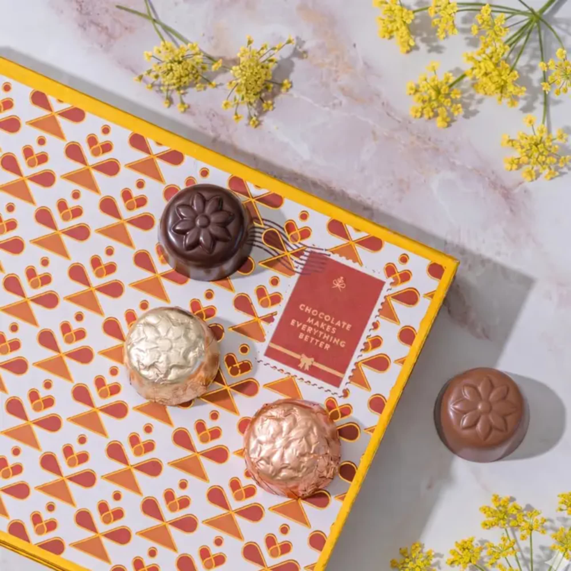 Box of assorted chocolates with yellow flowers nearby