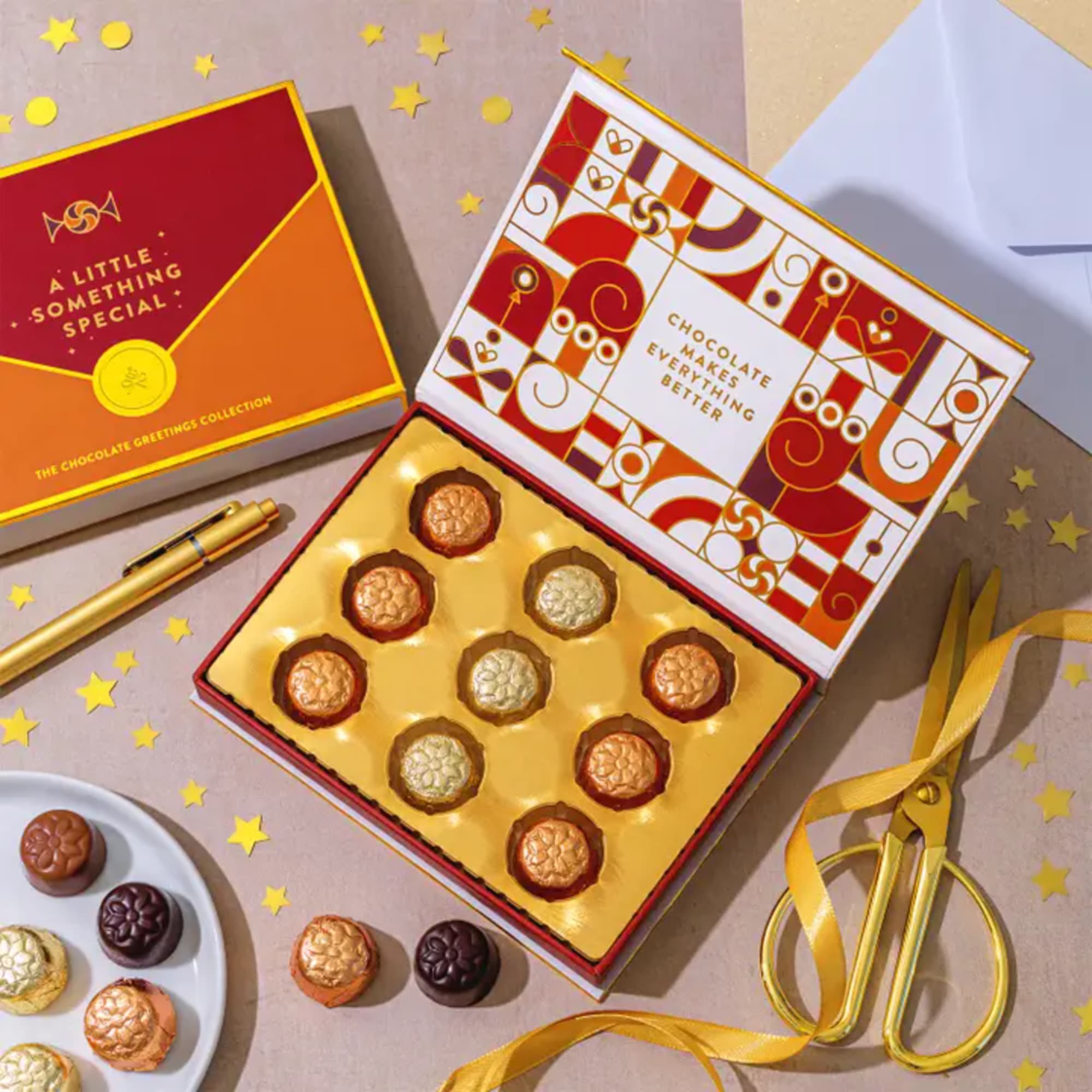 Box of assorted chocolates with gold ribbon and a decorative pen