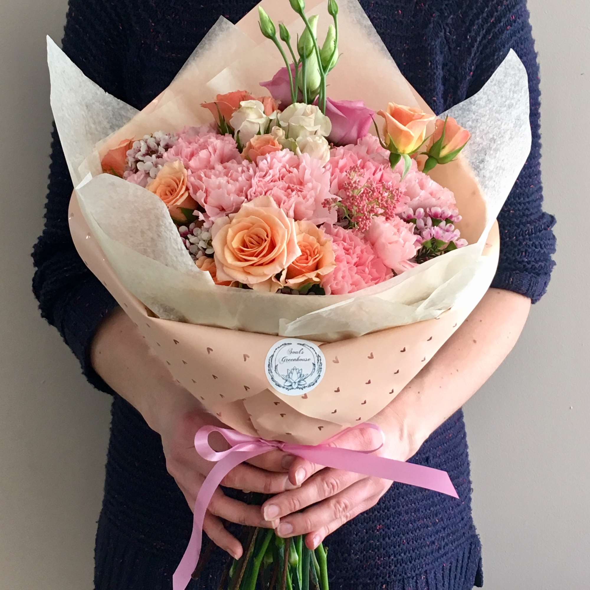 Handheld bouquet of pink and peach roses with pink blooms in paper wrap