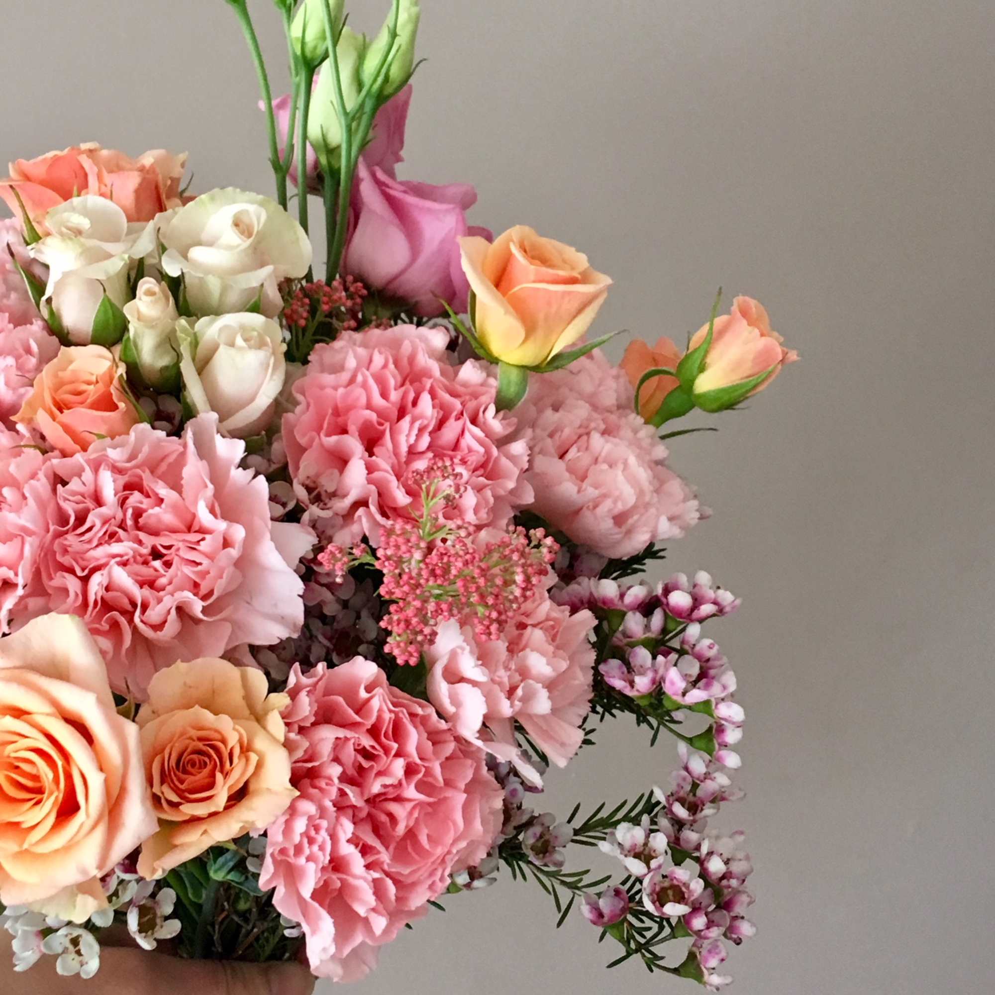 Handheld bouquet of pink and peach roses, carnations, and small white blooms