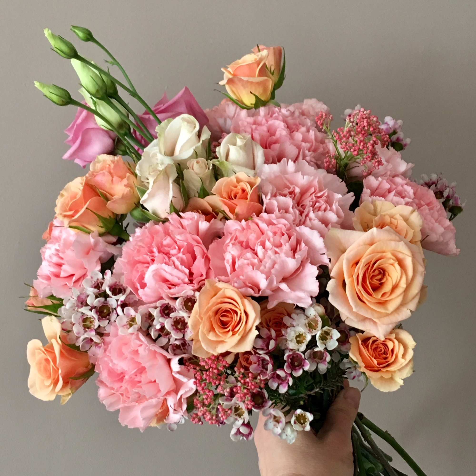 Handheld bouquet of pink and peach roses with carnations and small white blossoms